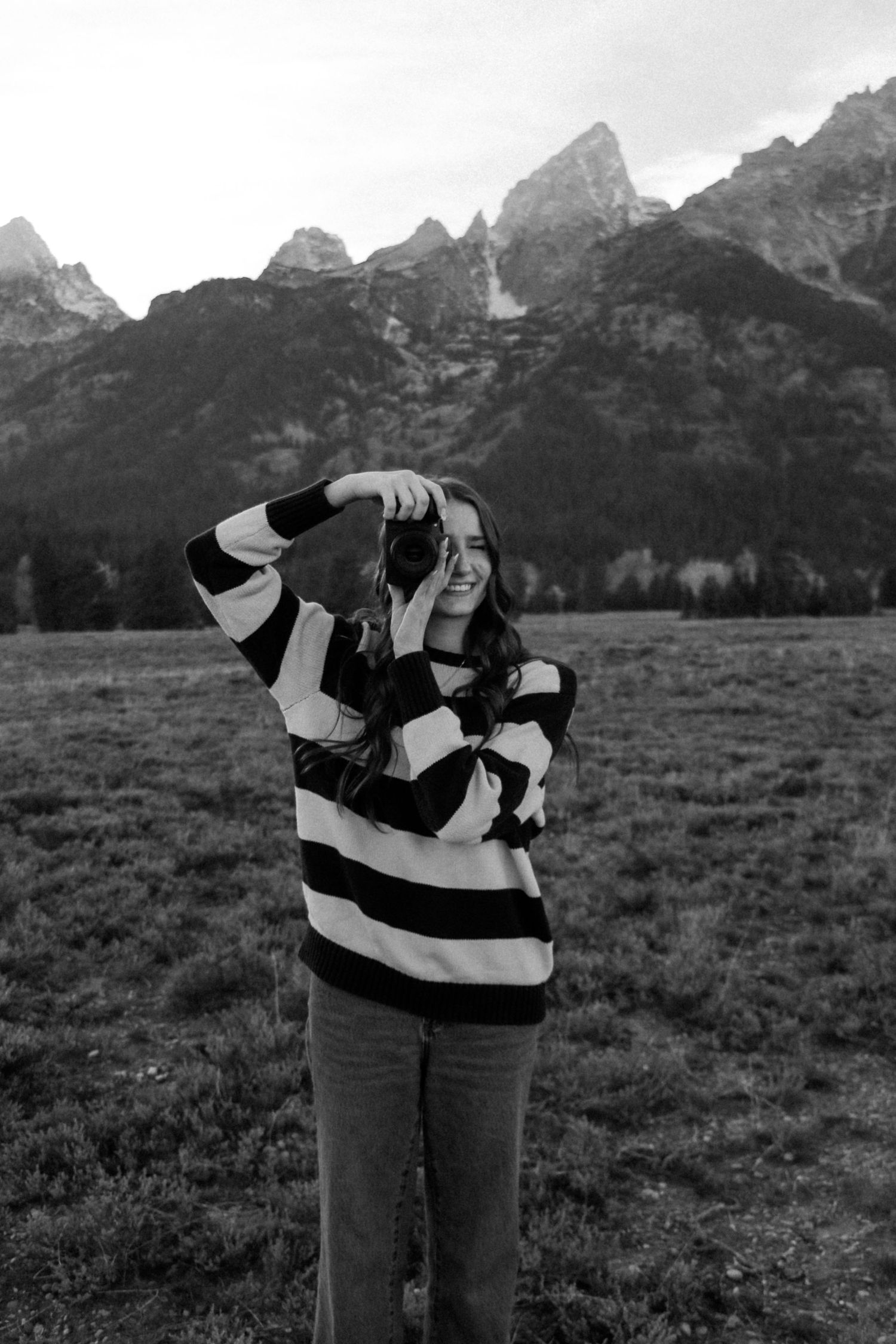 Black and white photo of someone taking pictures against a mountain backdrop.