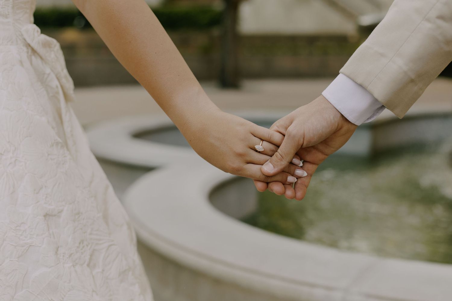 Close-up details of wedding couple's hands and dress on stone walkway.