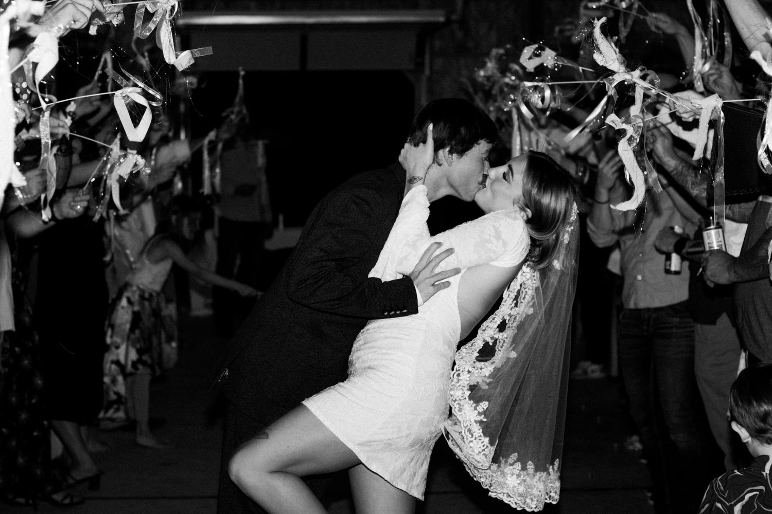 Joyful wedding reception crowd dancing and celebrating on a dark dance floor with festive lighting.