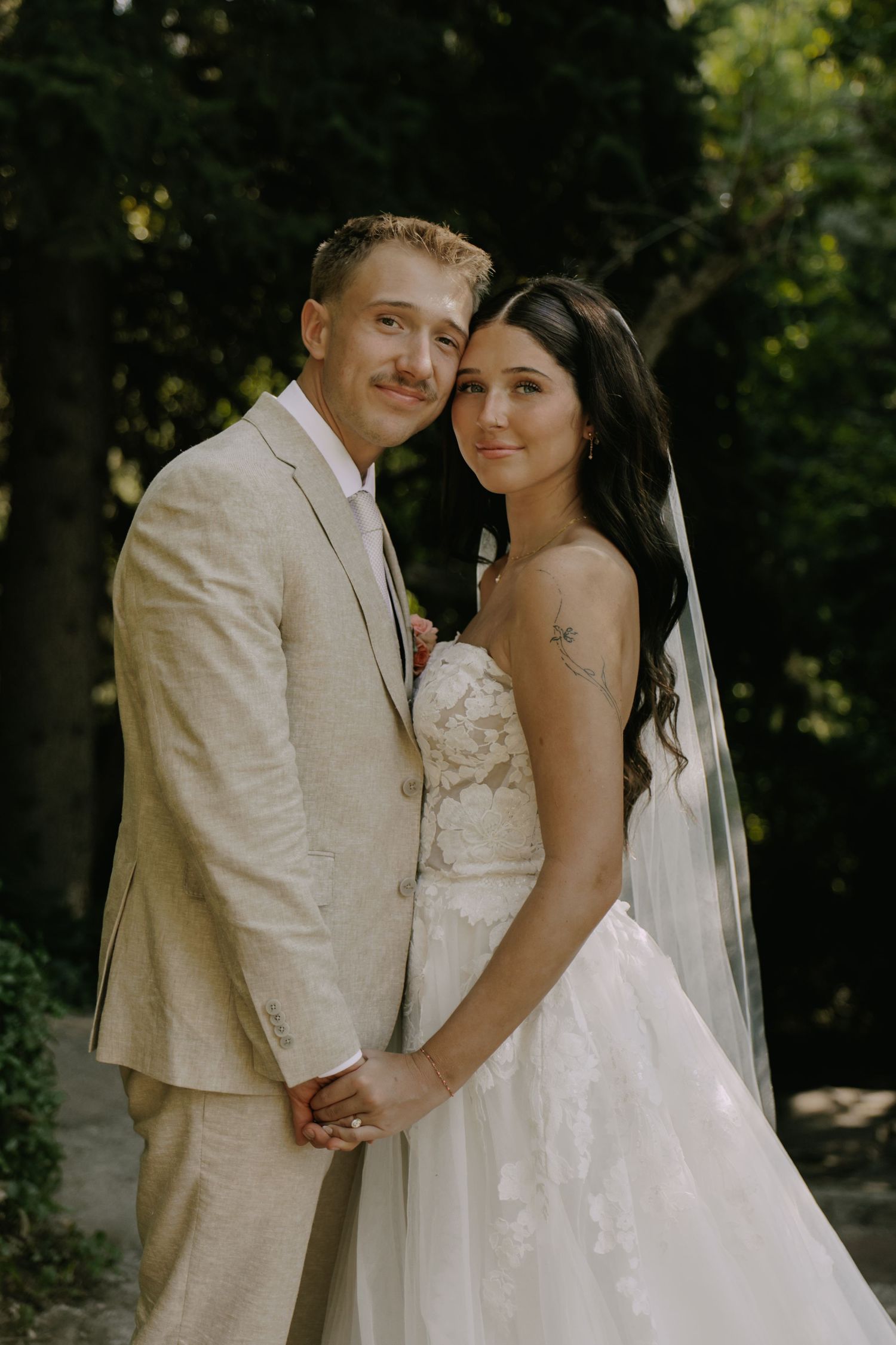 Newlyweds in cream and white wedding attire posing in garden setting.