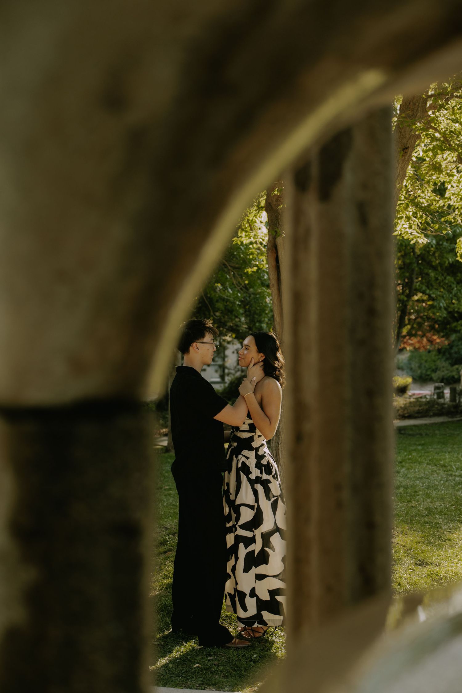 Romantic couple embracing in garden setting framed by architectural elements.
