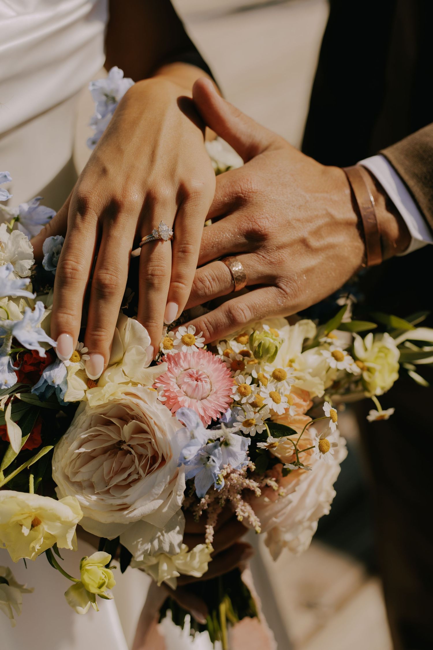 Close-up of newlyweds' hands with rings and wedding bouquet.