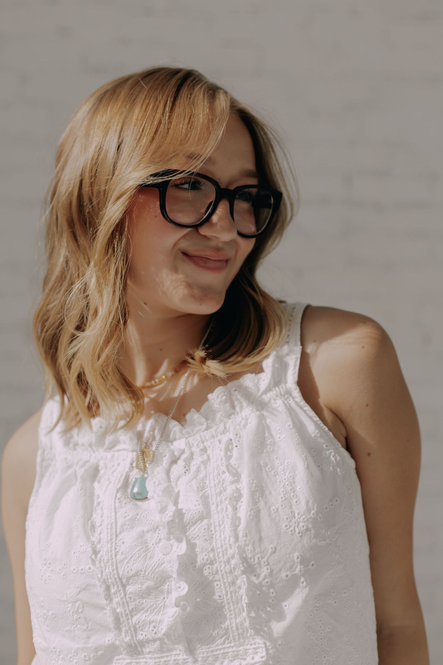 Person wearing white lace sleeveless top and glasses in natural lighting.