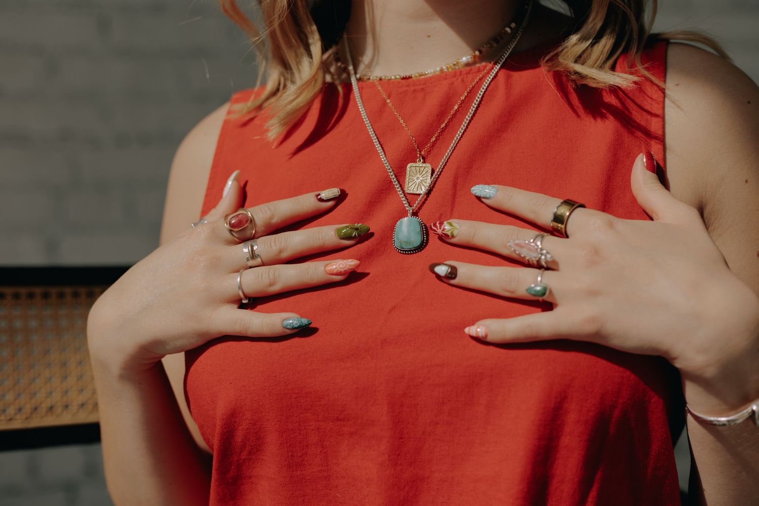 Close-up detail of hands wearing multiple rings against a red clothing background.