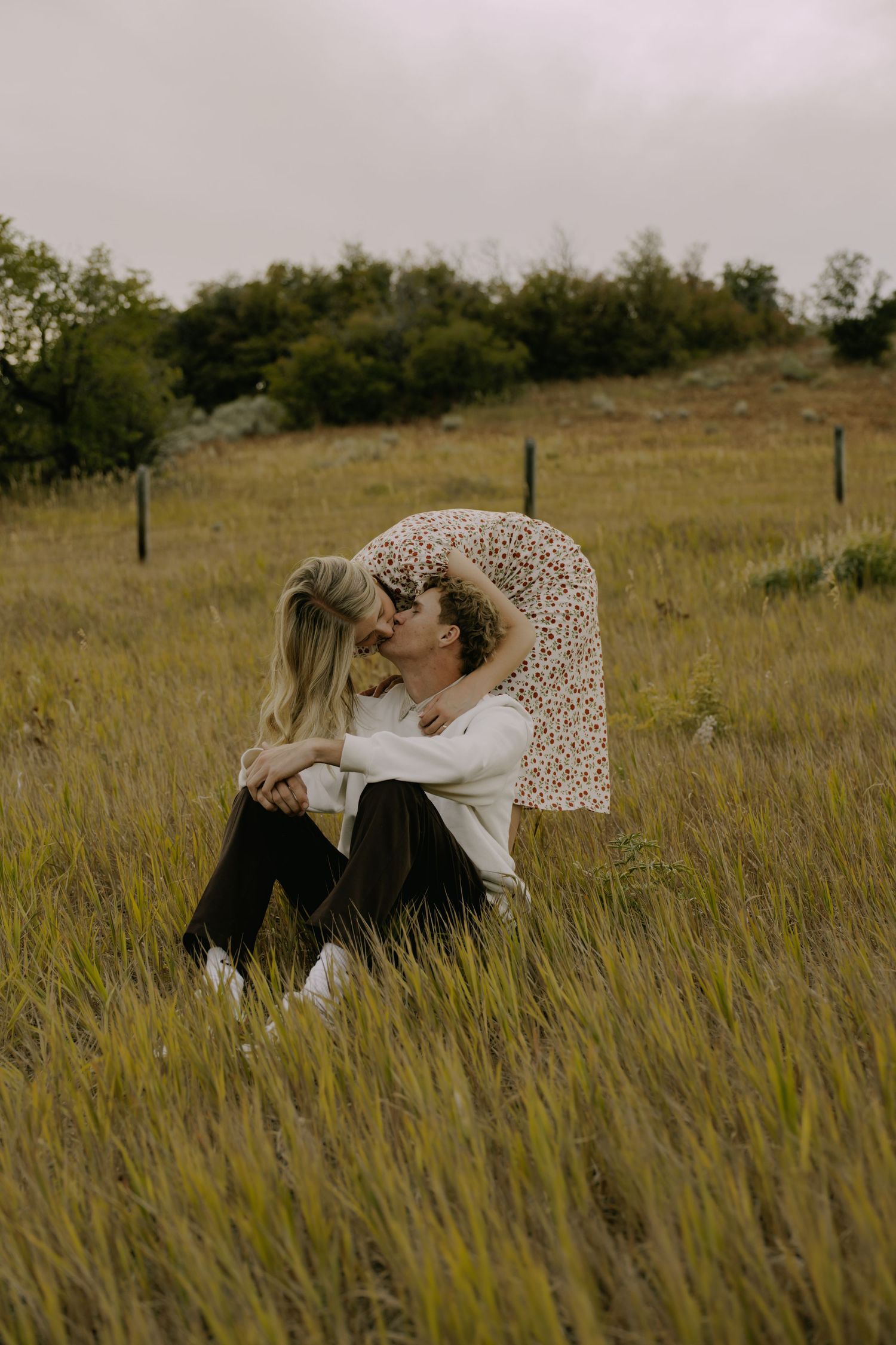 A couple shares intimate moments in a golden field with mountains in the distance.