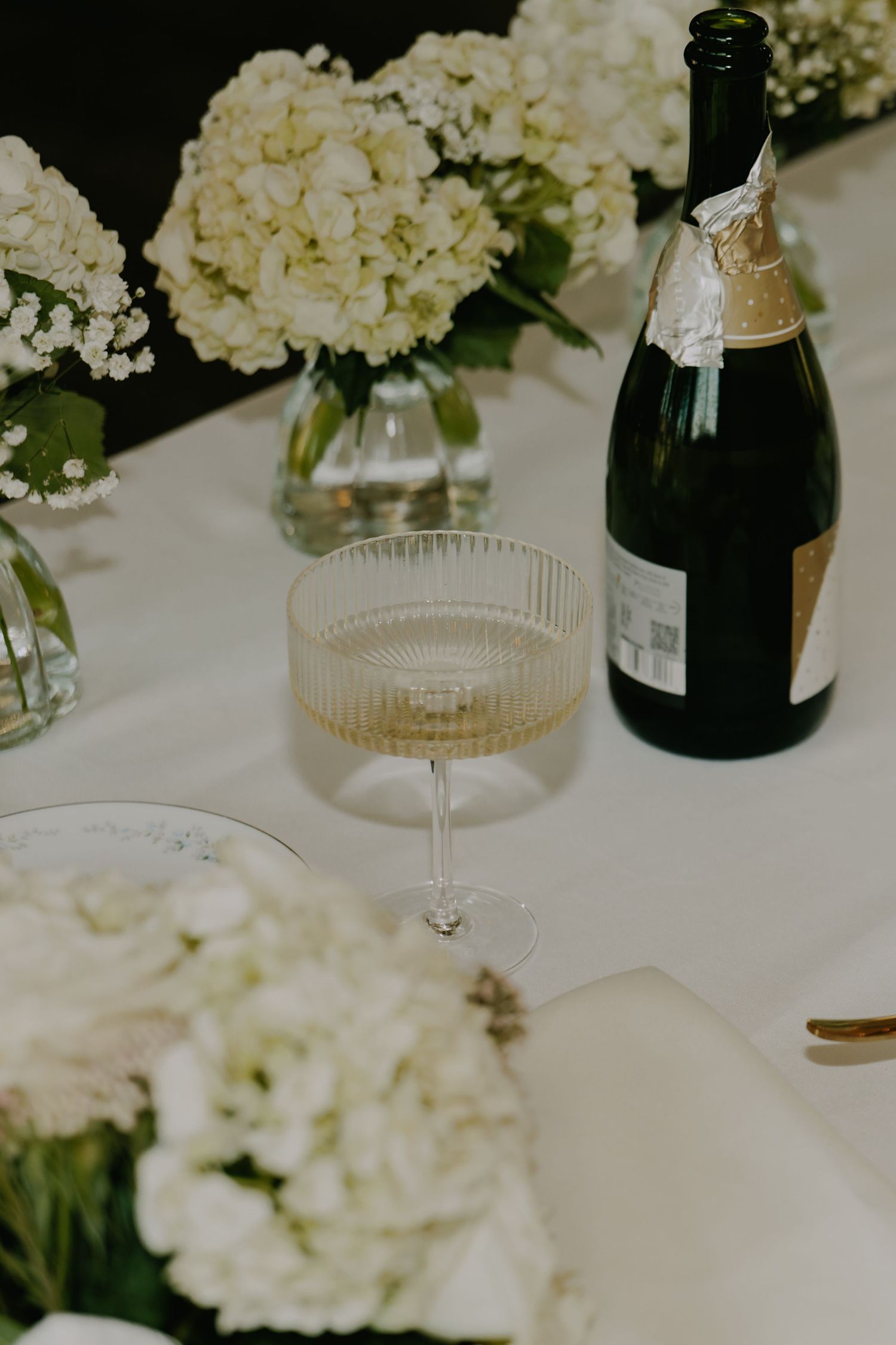 White hydrangea centerpieces with champagne bottle and crystal glassware on elegant table setting.