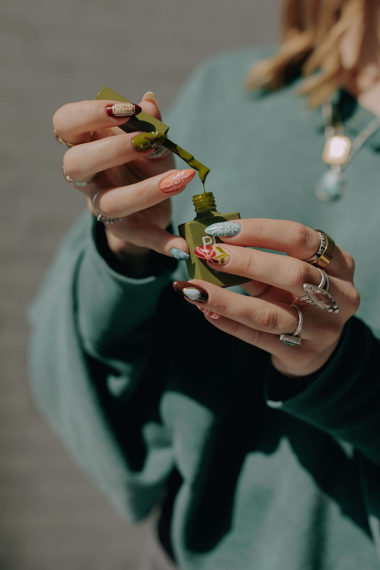 Close-up of manicured hands with rings examining small bottles in natural light.