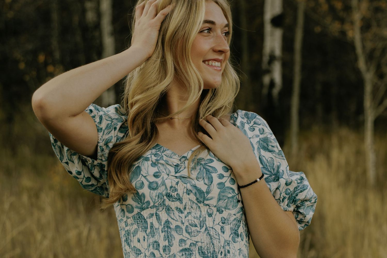 A floral blue and white dress is showcased in a golden autumn field with aspen trees in the background.