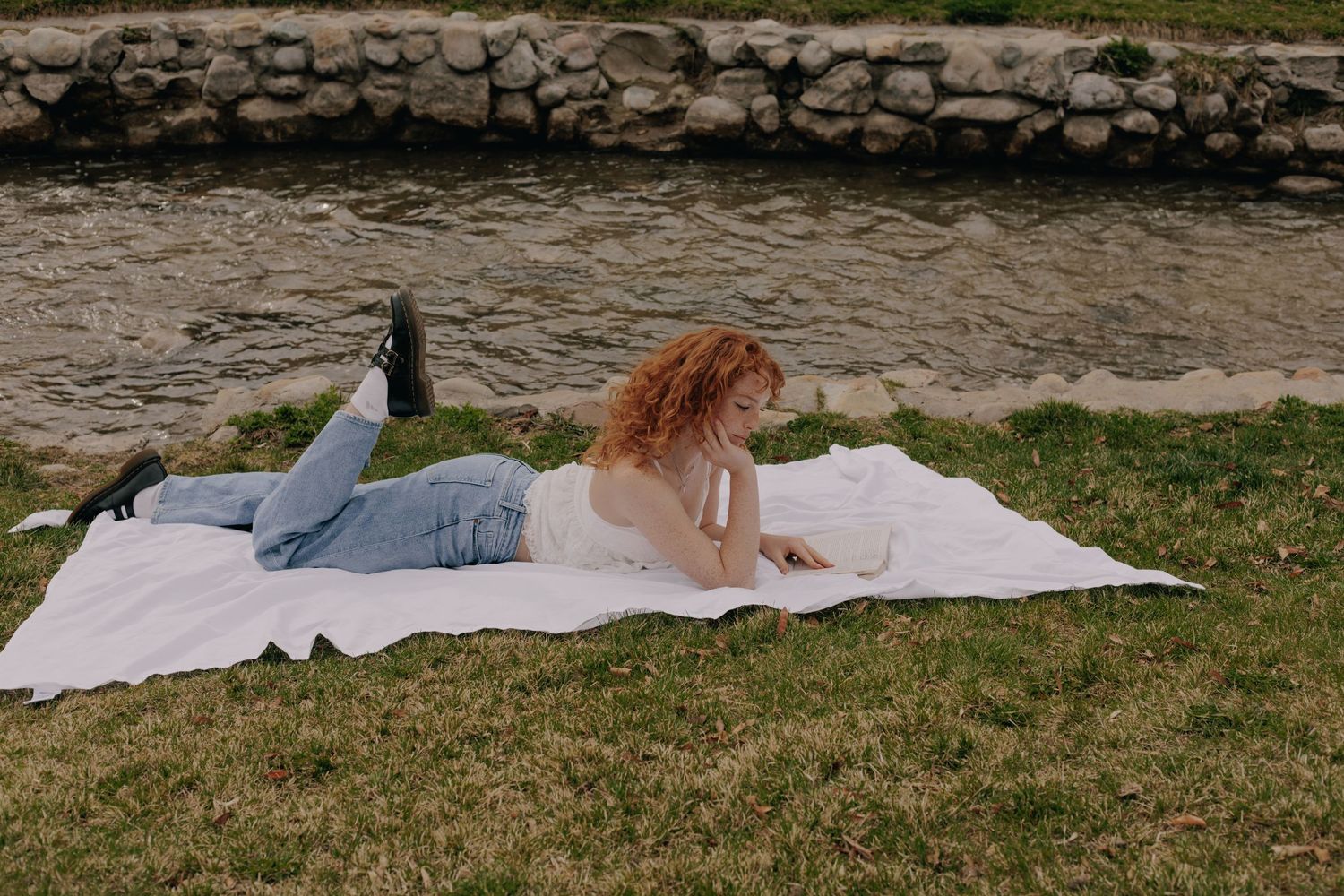 Person resting on blanket near stone-lined waterfront.