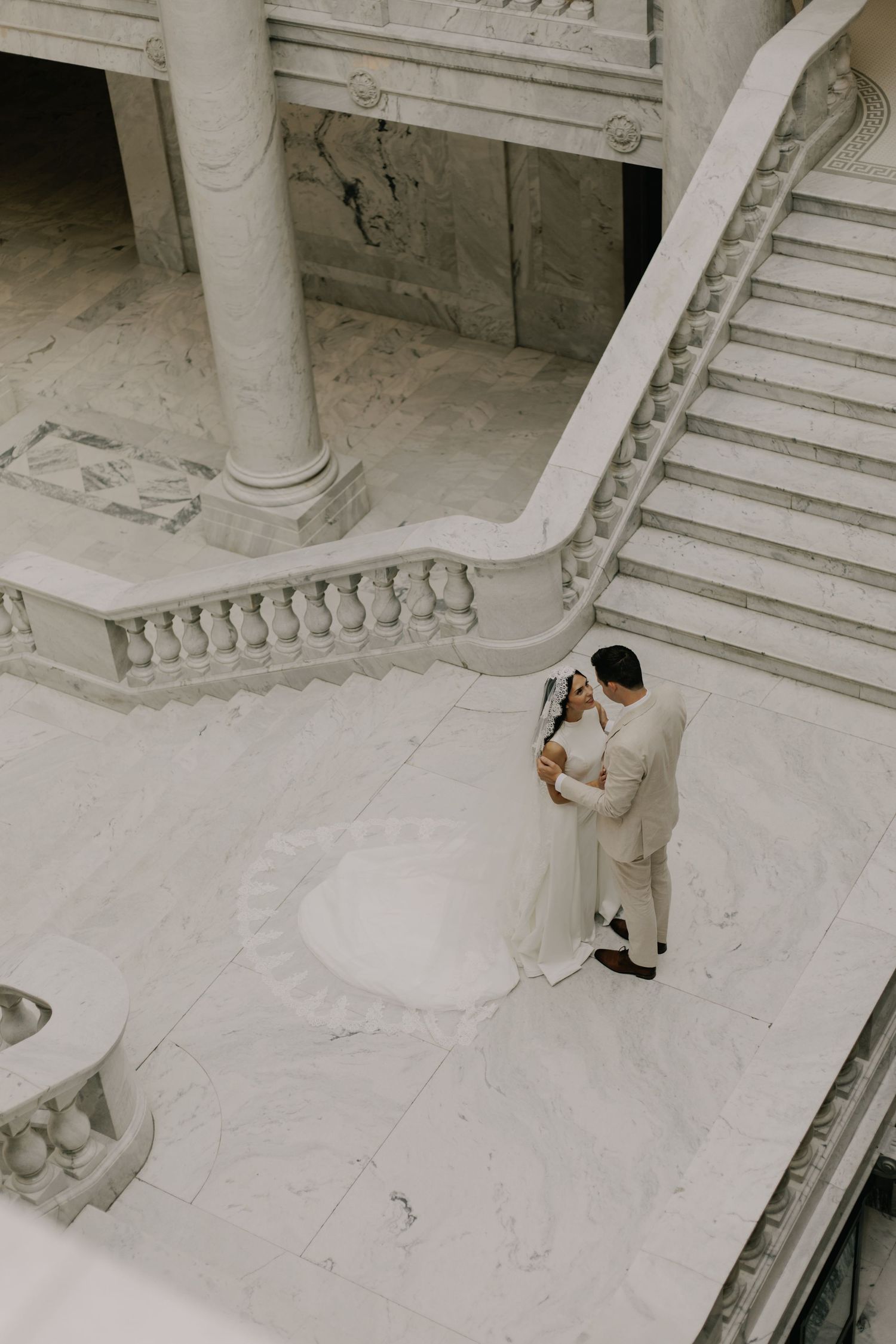 Aerial view of a couple embracing on grand marble staircase in formal attire.