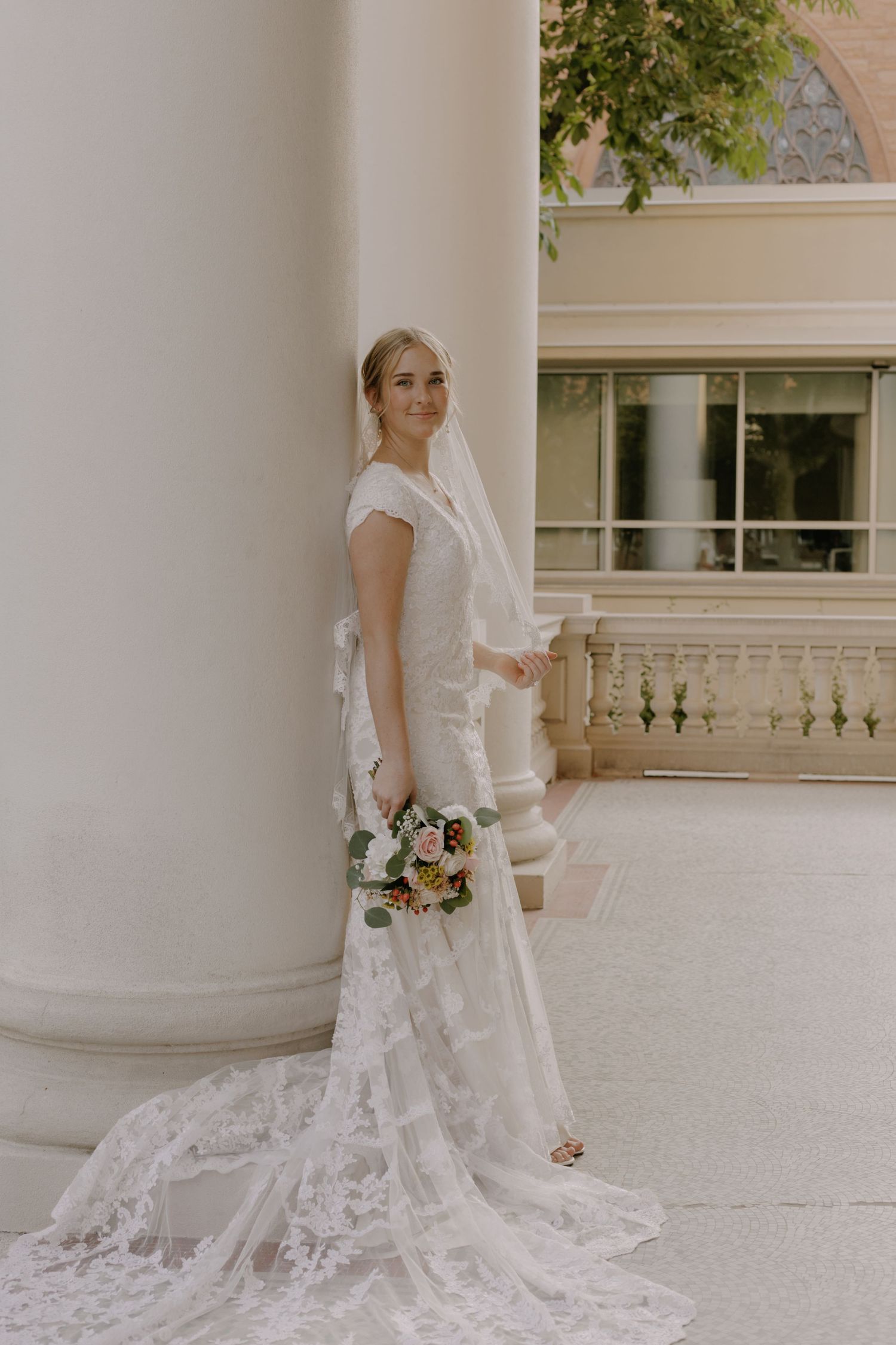 Bride in lace gown posing between elegant white columns.