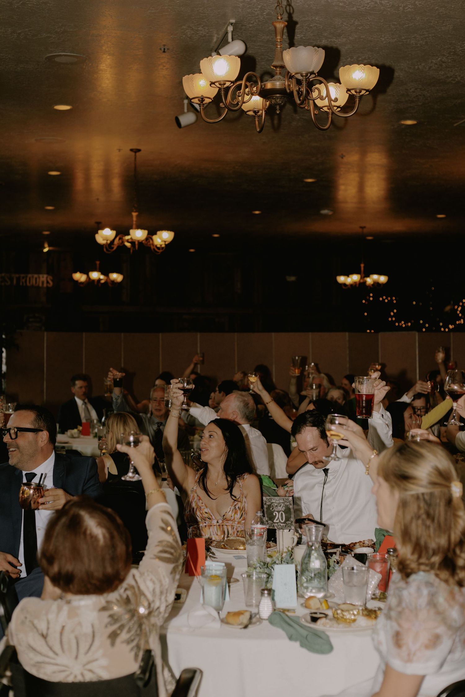 Wedding reception guests celebrating with raised arms in dimly lit venue.