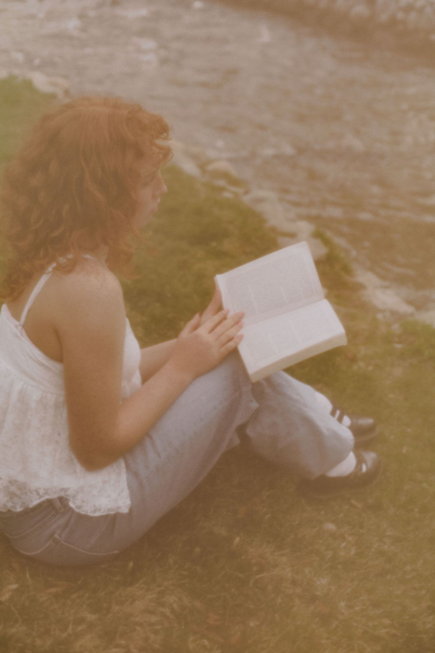 Person in white dress reading book while lounging outdoors.