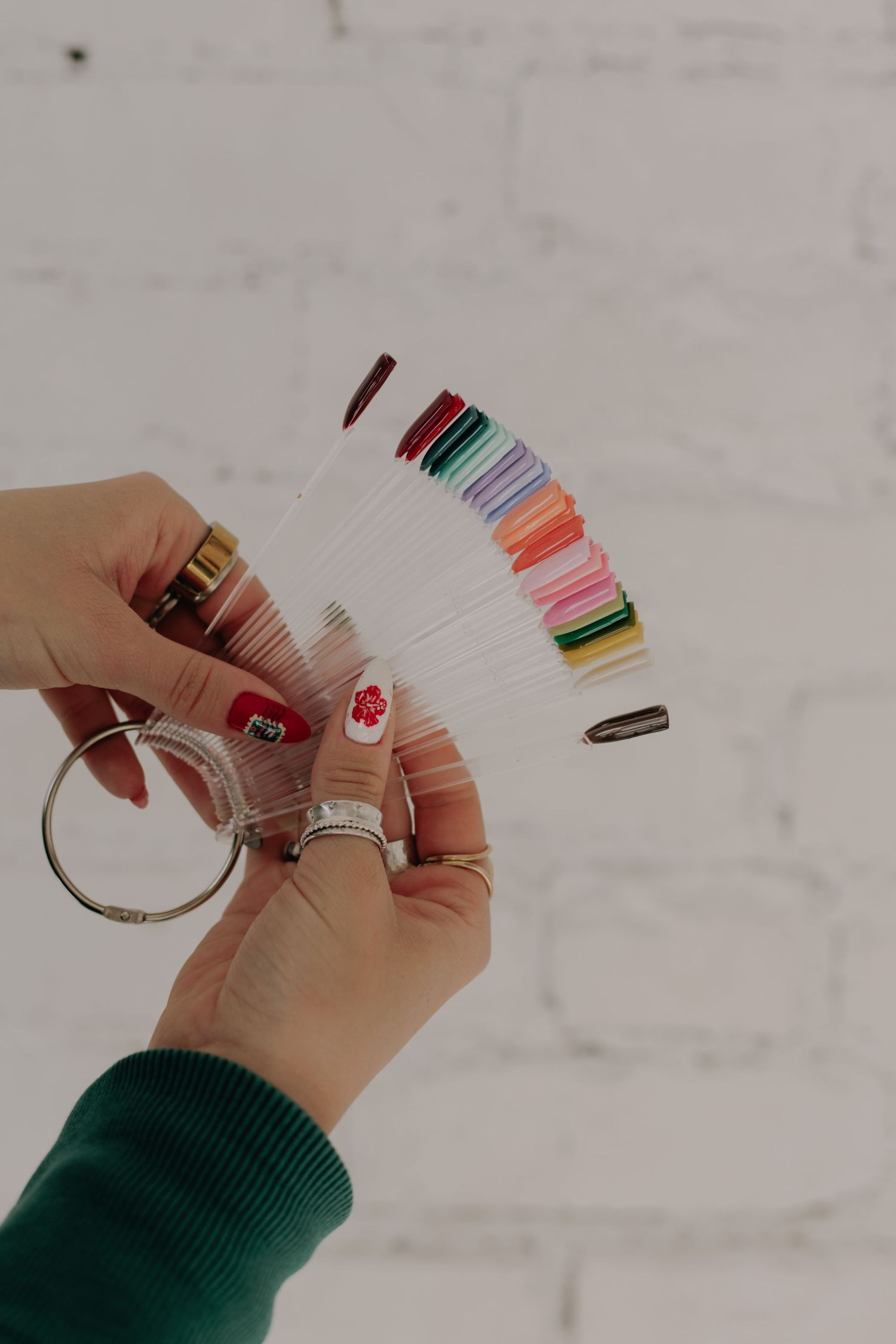 Close-up of hands holding colorful nail polish swatches against a white background.