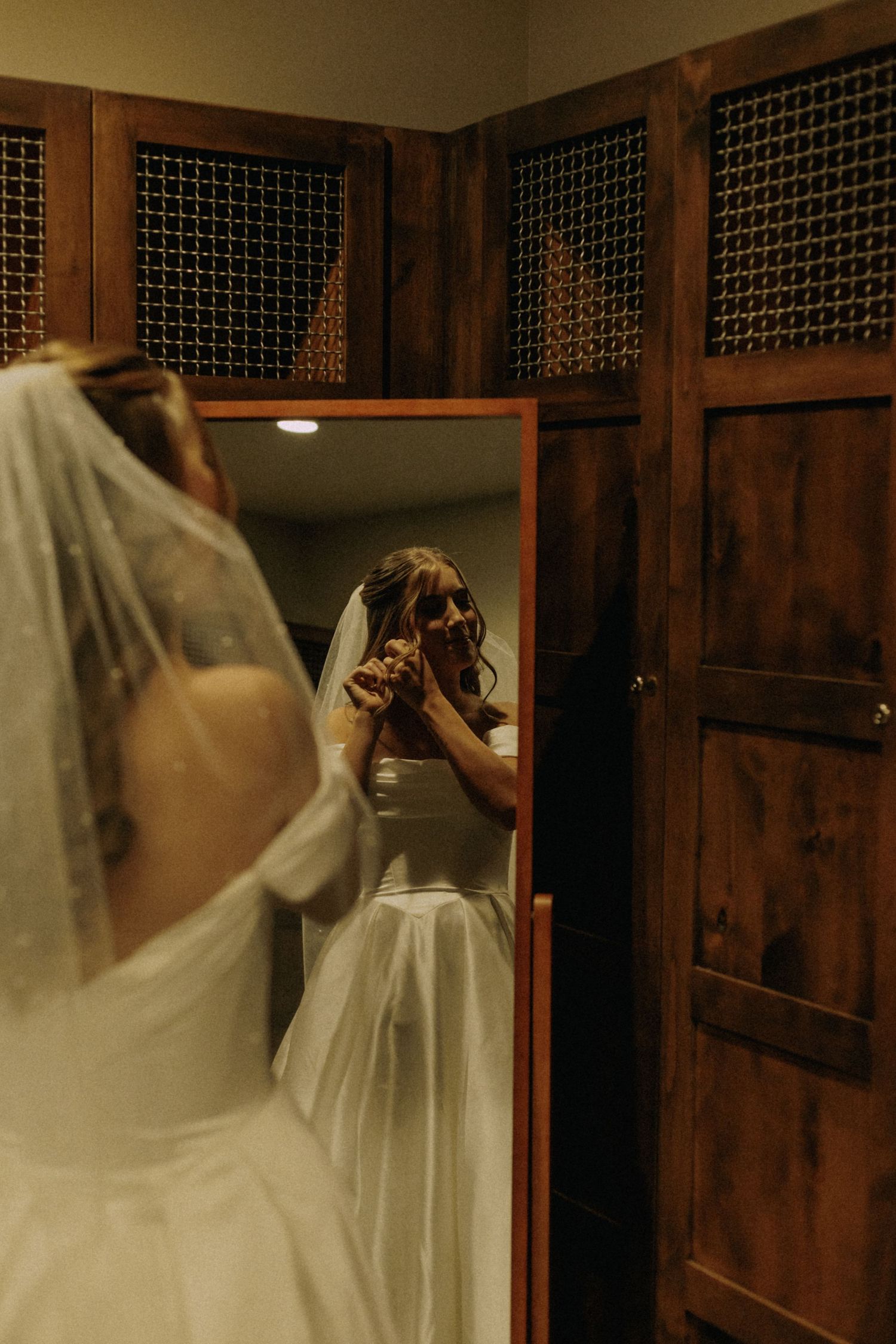 Wedding dress hanging in rustic wooden dressing room with mirror reflections.