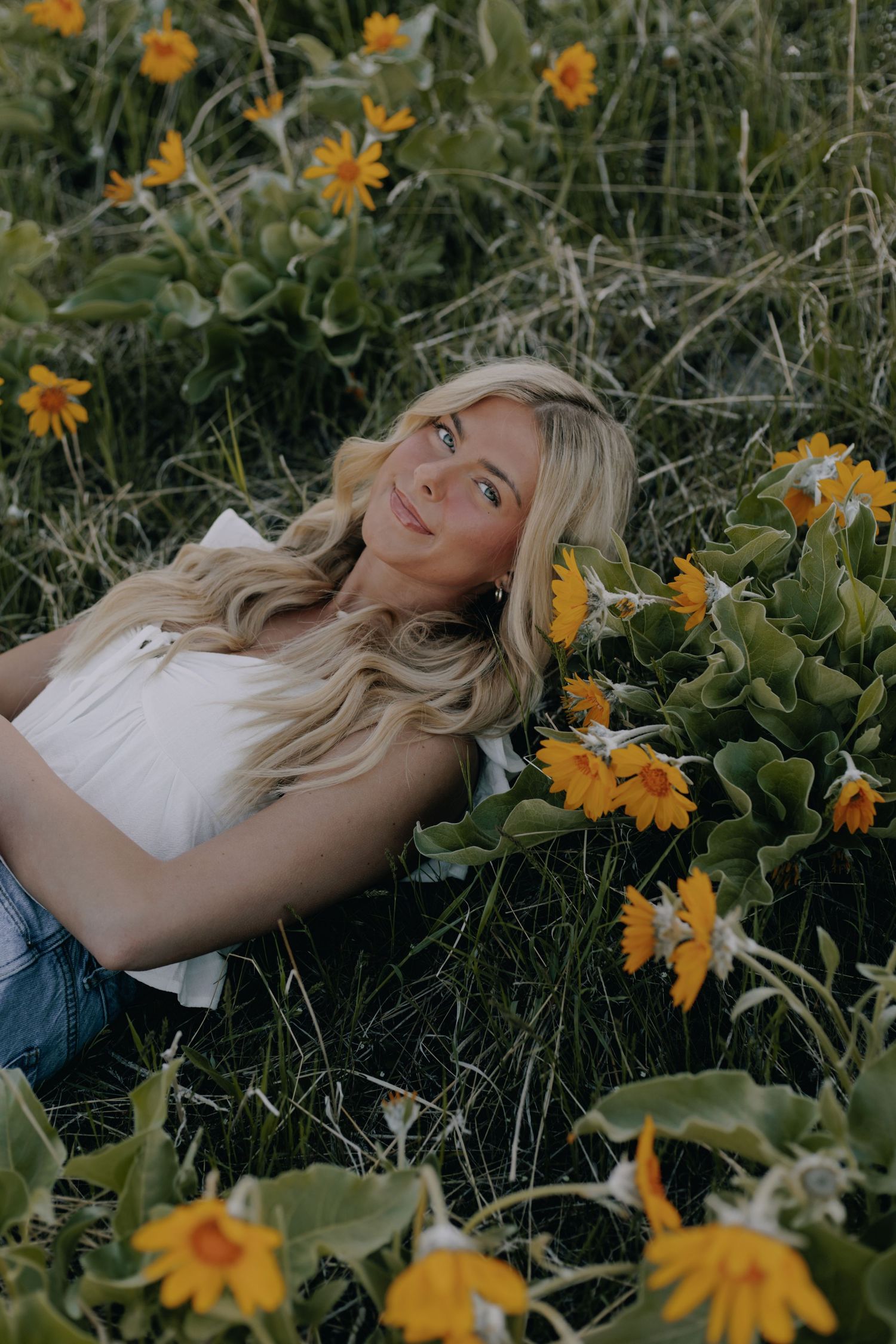 Woman lying in field of yellow wildflowers during golden hour photography session.