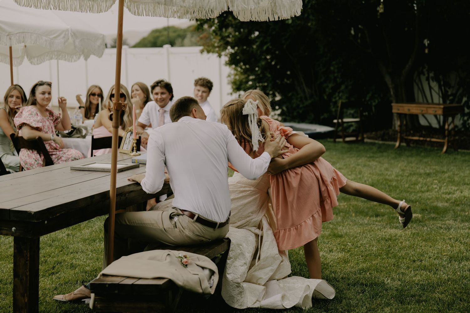 Wedding guests enjoy an outdoor celebration on a sunny day with green grass and trees in the background.