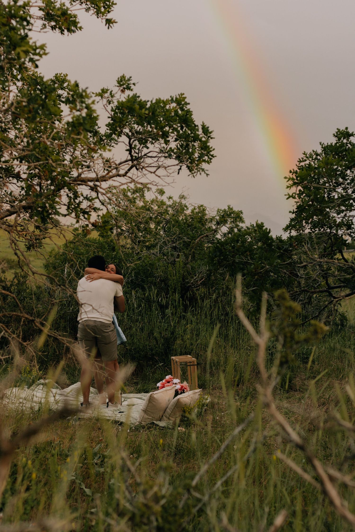 A beautiful rainbow appears in the sky over a grassy field during an outdoor photoshoot.
