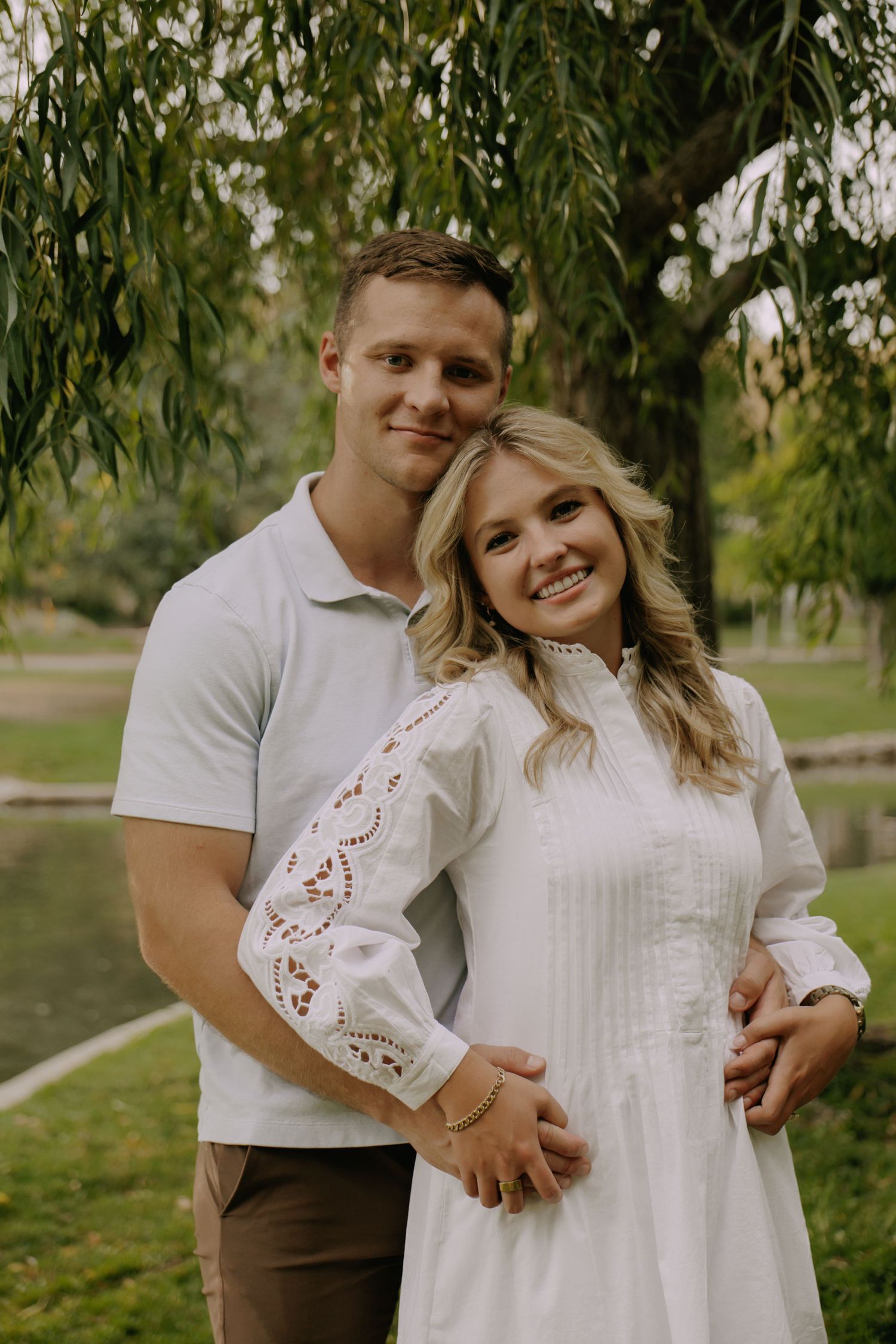 Romantic couple poses together under a weeping willow tree in a park setting.