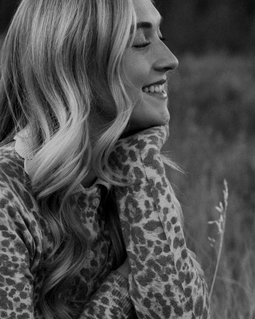 Black and white portrait of woman in leopard print sweater smiling with eyes closed.