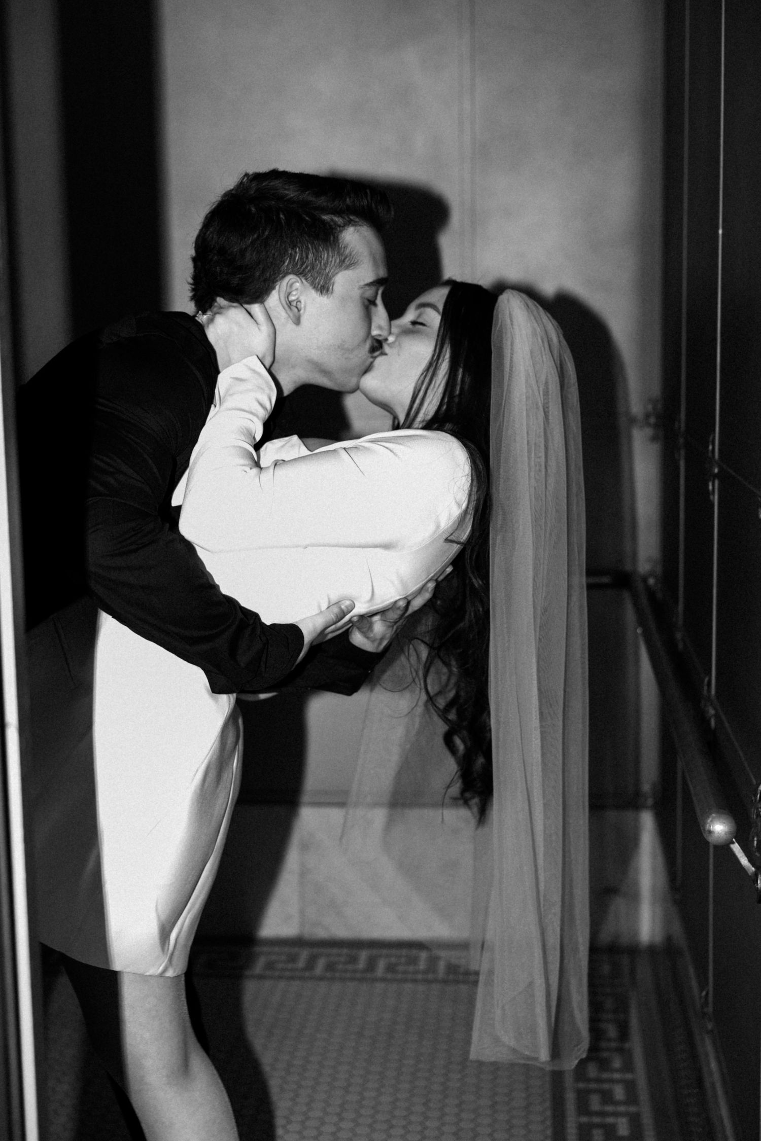 A dramatic black and white photograph captures an intimate embrace in a hallway.