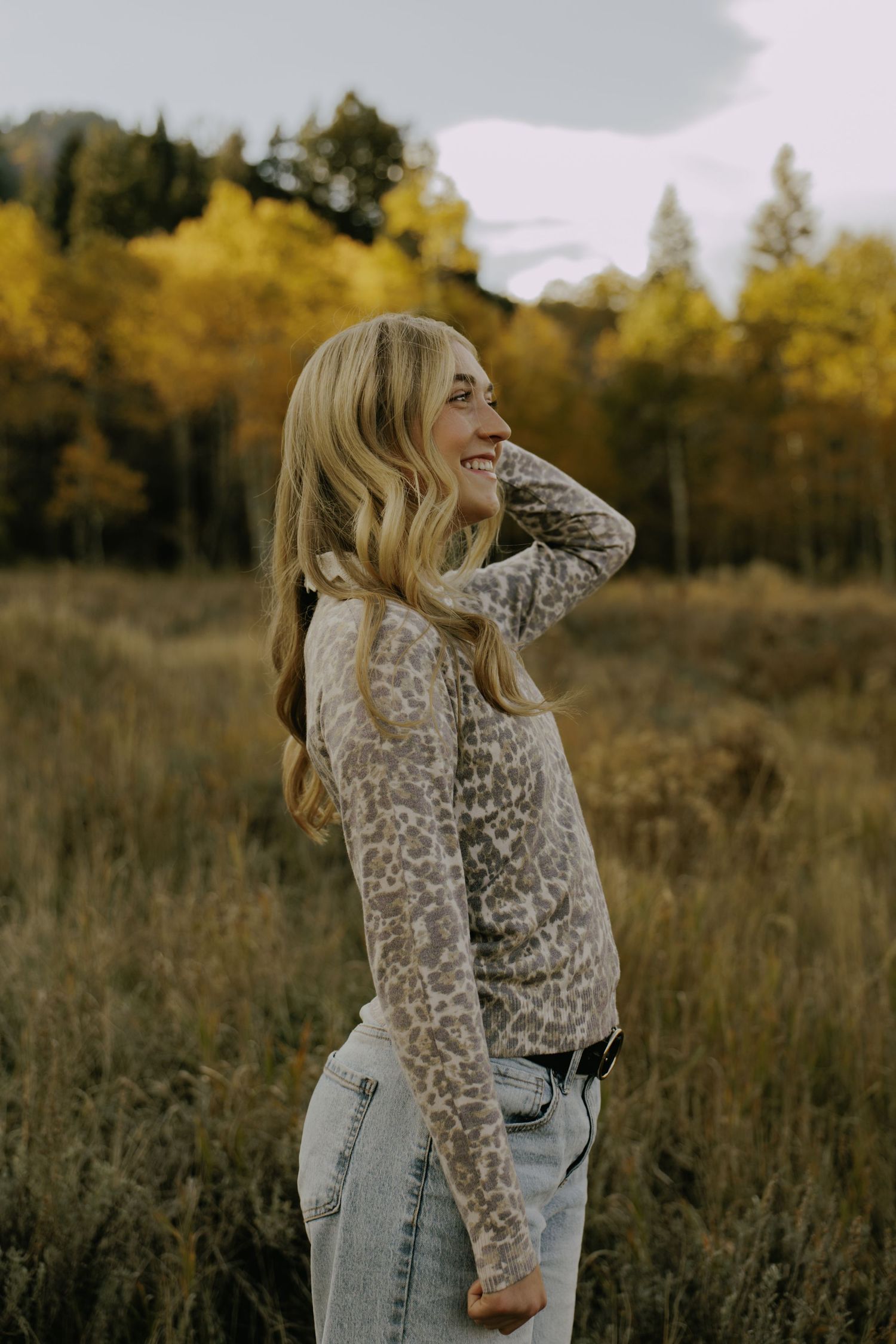 Woman in leopard print top laughs joyfully in fall meadow setting.