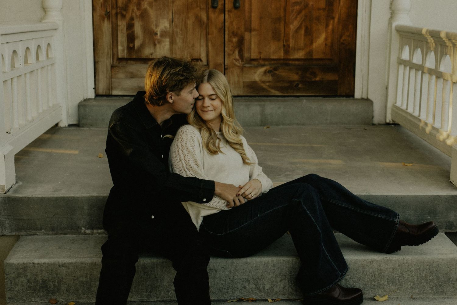 Couple sharing intimate moment on vintage porch steps during fall season.