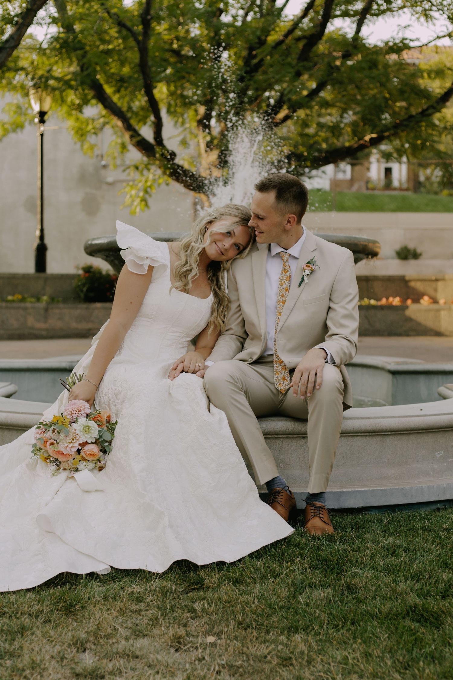 Wedding couple poses together on grass with beautiful garden backdrop.