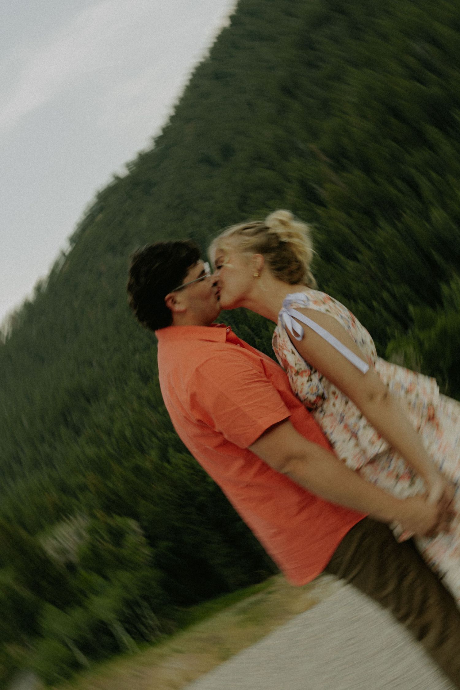 A couple sharing tender moments against a forested mountain backdrop at dusk.