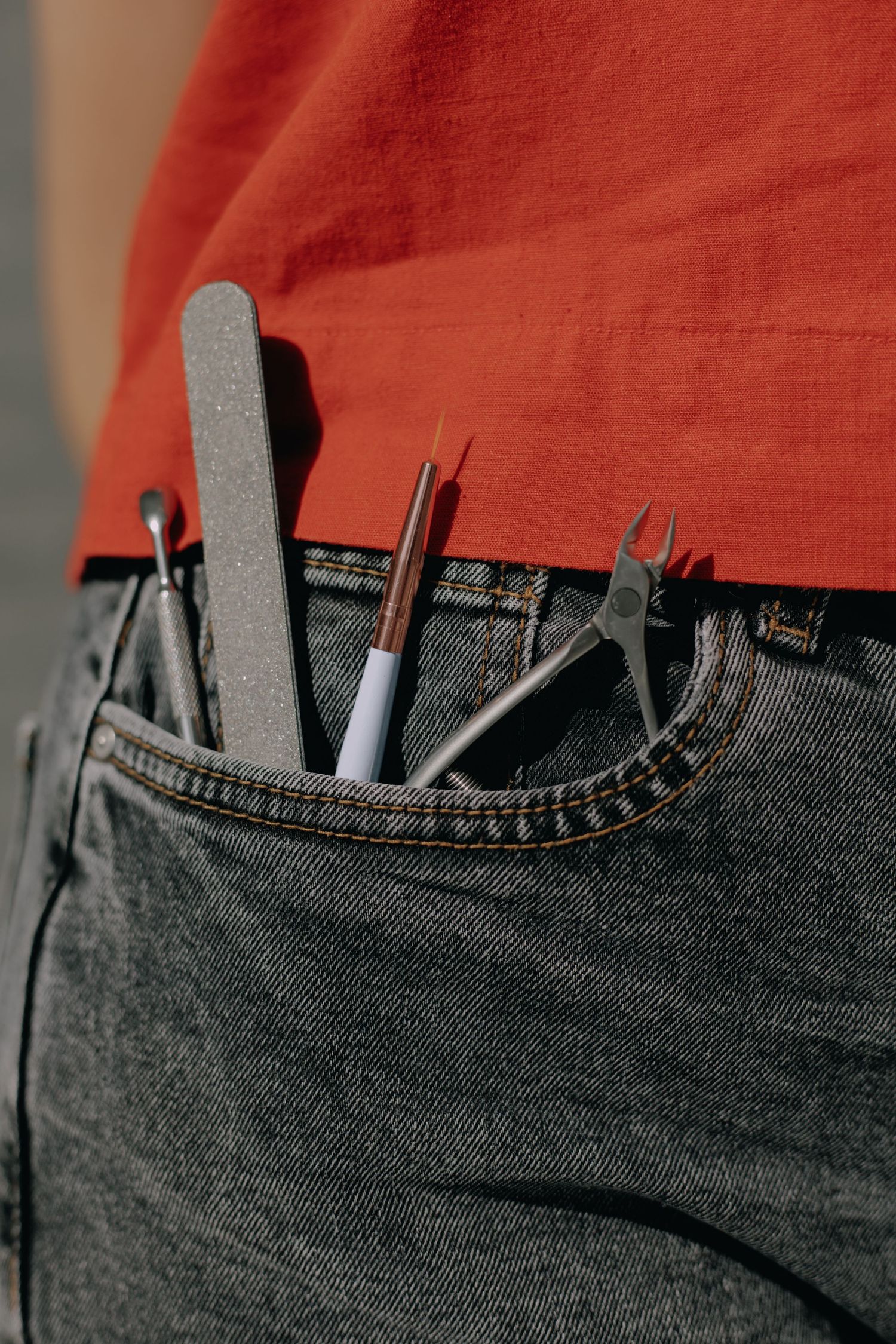 Nail care tools and implements tucked into denim jeans pocket with orange fabric above.