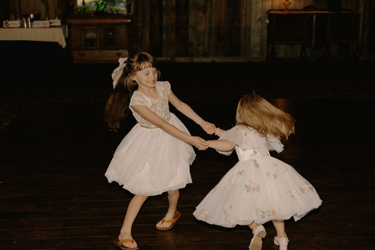 Young flower girls in white dresses dancing at wedding reception.
