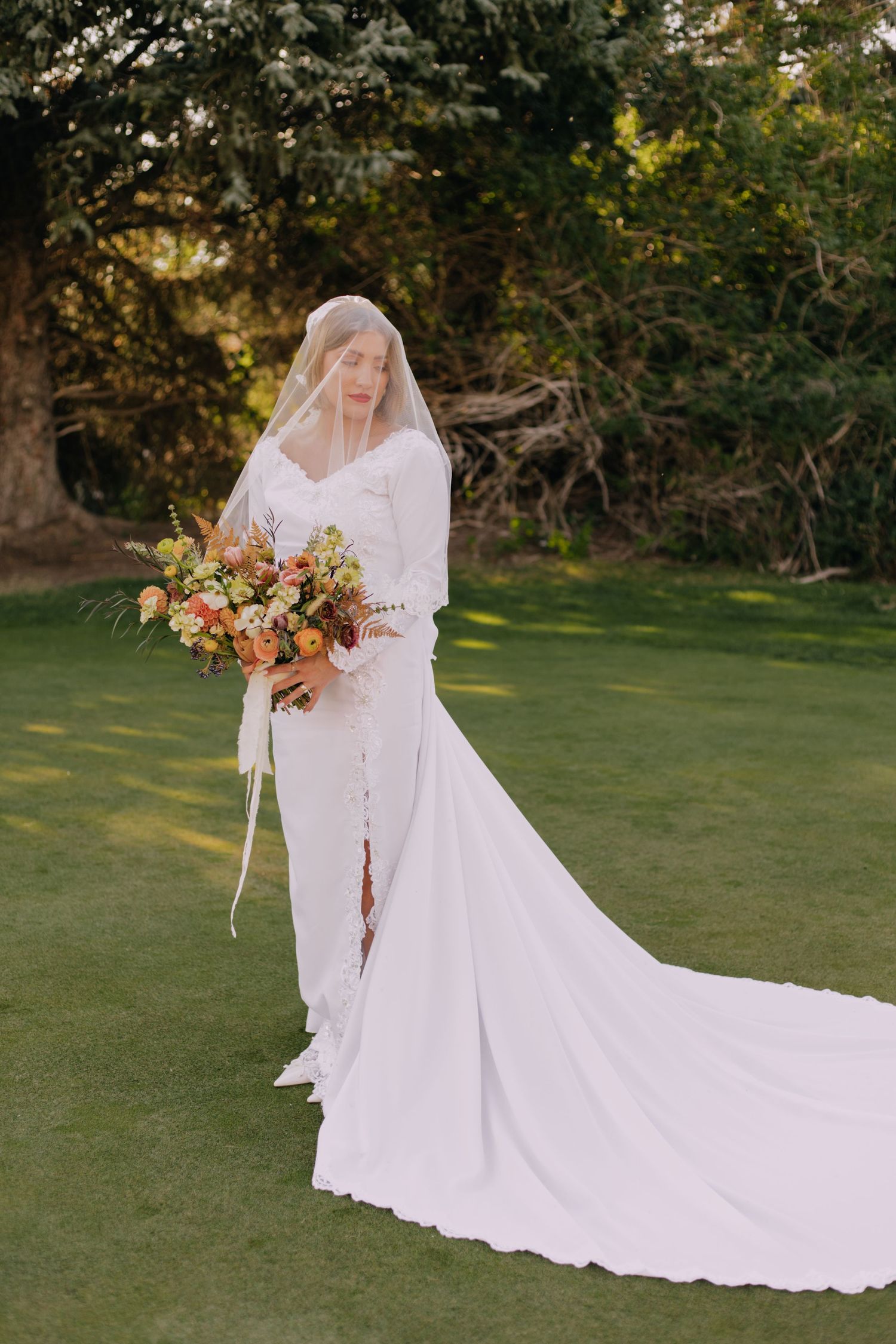 Elegant white wedding dress with flowing train displayed in an outdoor garden setting at sunset.