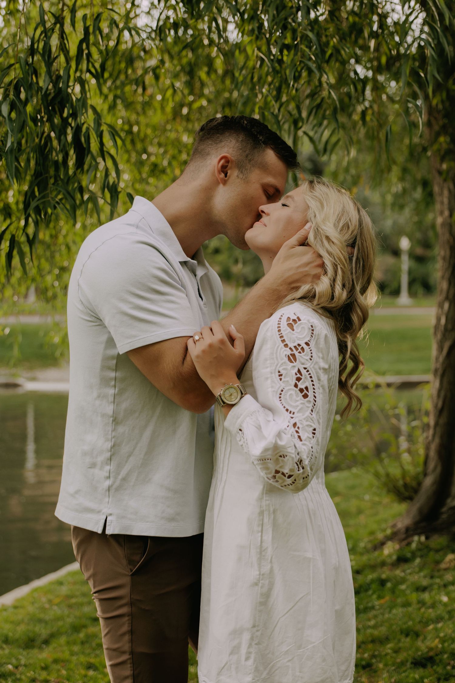 Romantic couple sharing an intimate moment under willow branches near water.