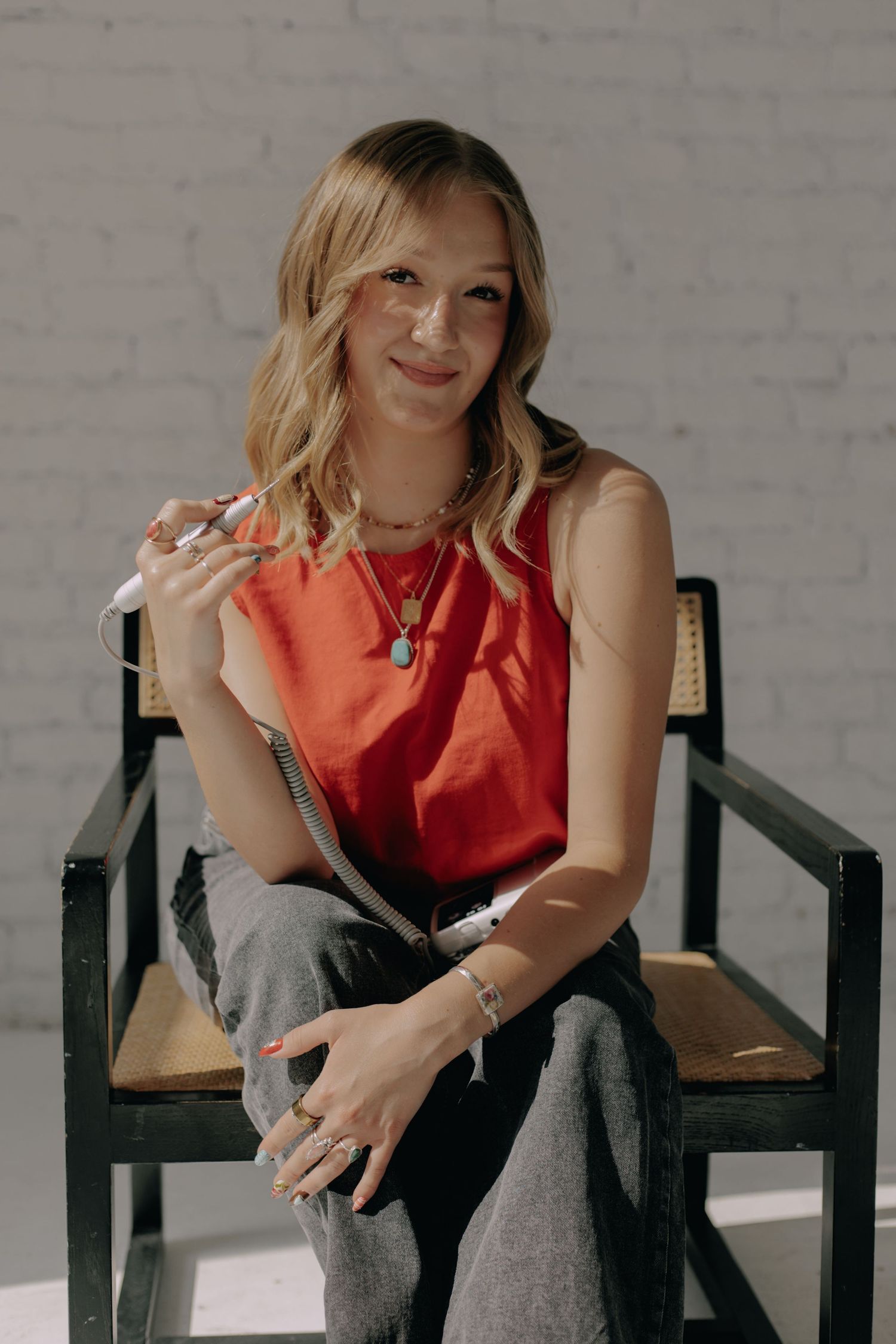 Relaxed portrait in red sleeveless top against white brick background.