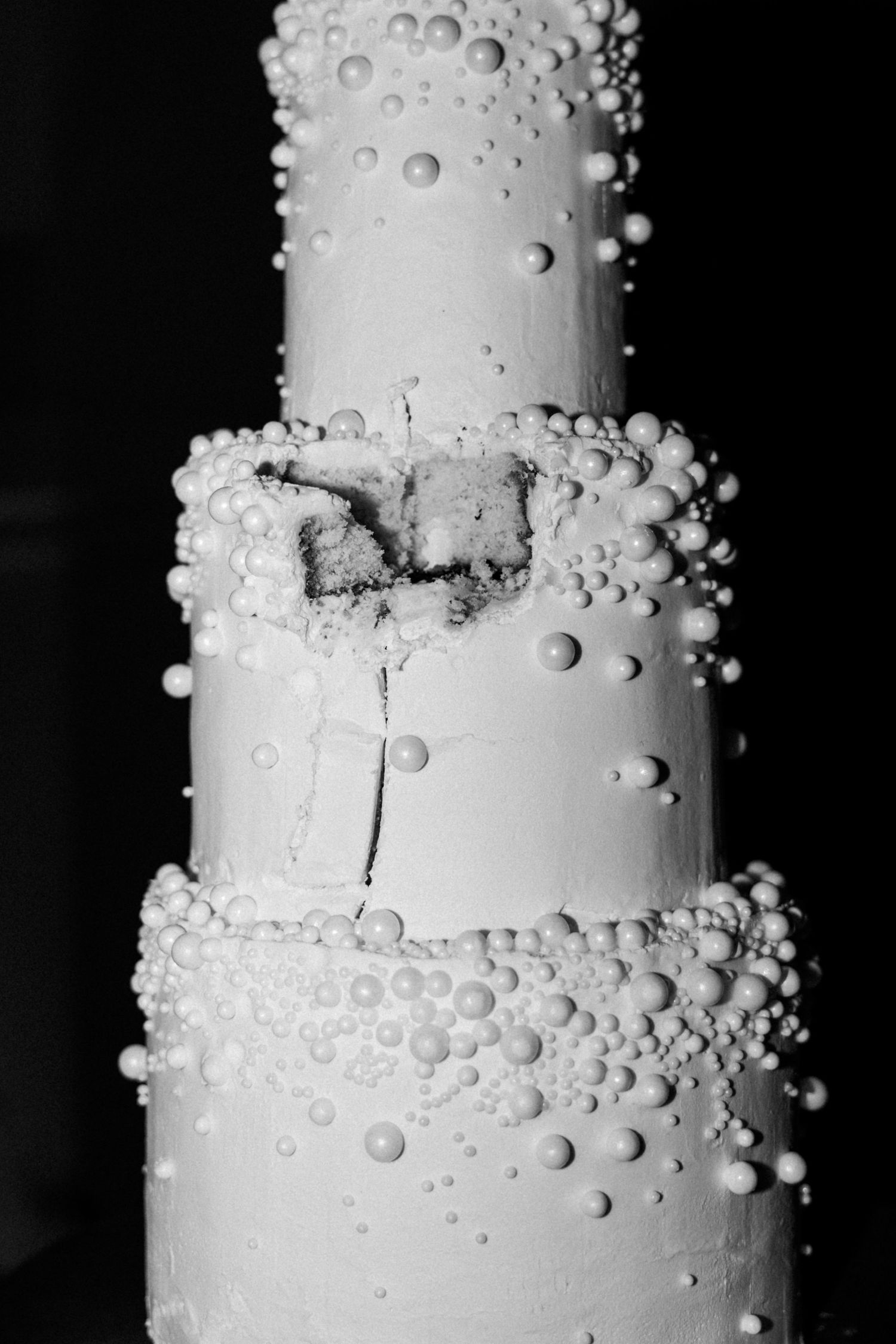 Elegant white wedding cake decorated with delicate pearl-like details against black background.
