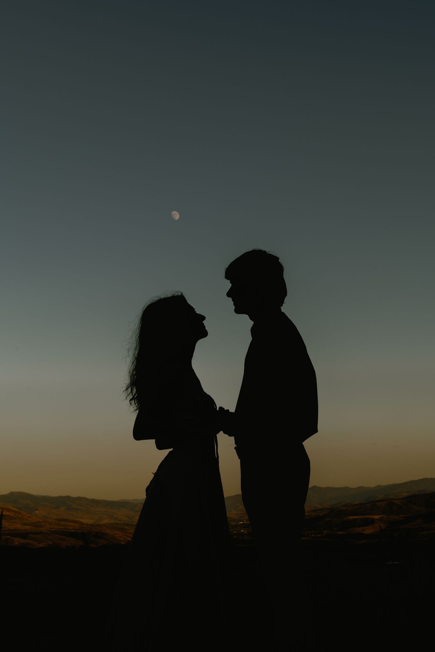 Silhouettes of a couple against a dusky sky with mountains in the background.