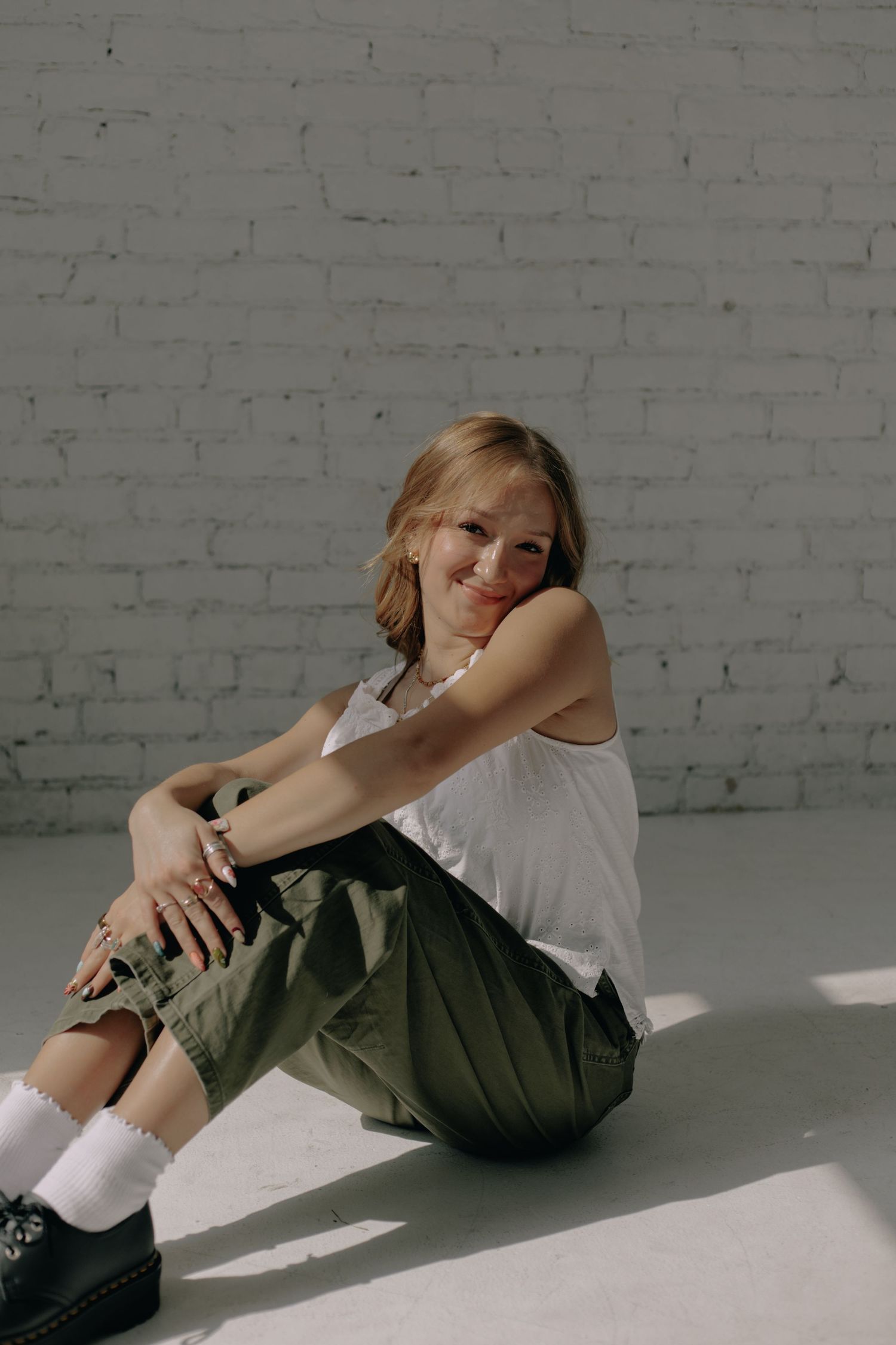 Figure lounging on floor wearing casual white top and cargo pants in minimalist setting.