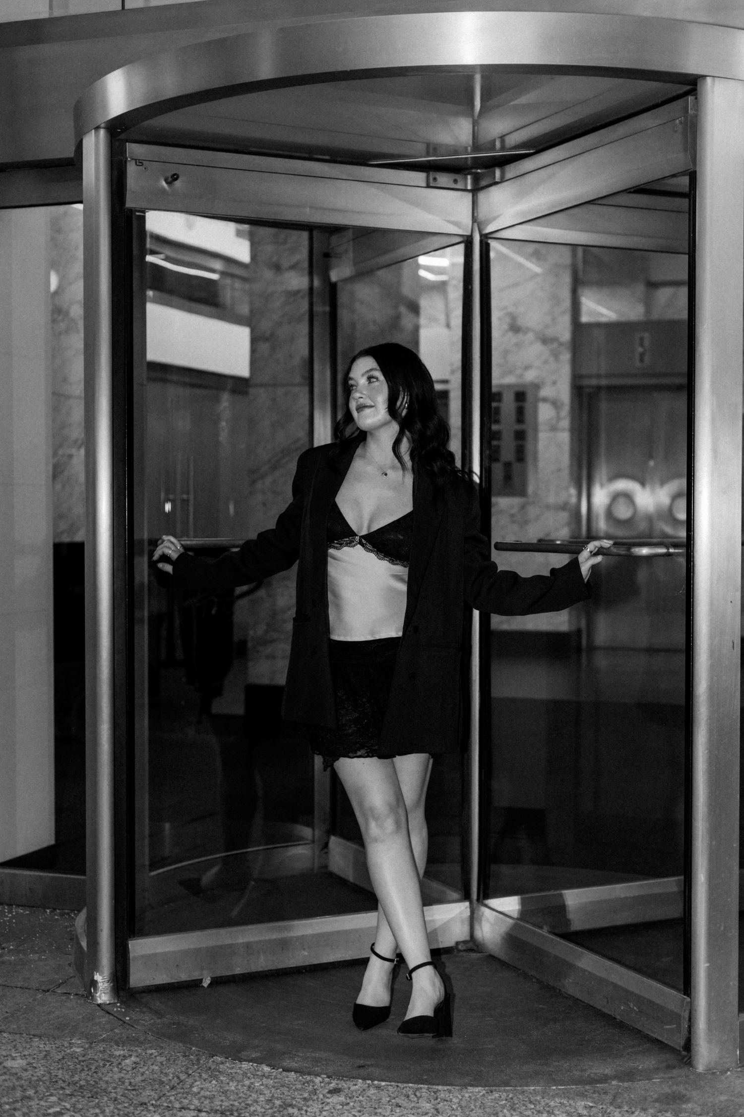 A stylish figure poses dramatically in a revolving door at a modern building entrance.