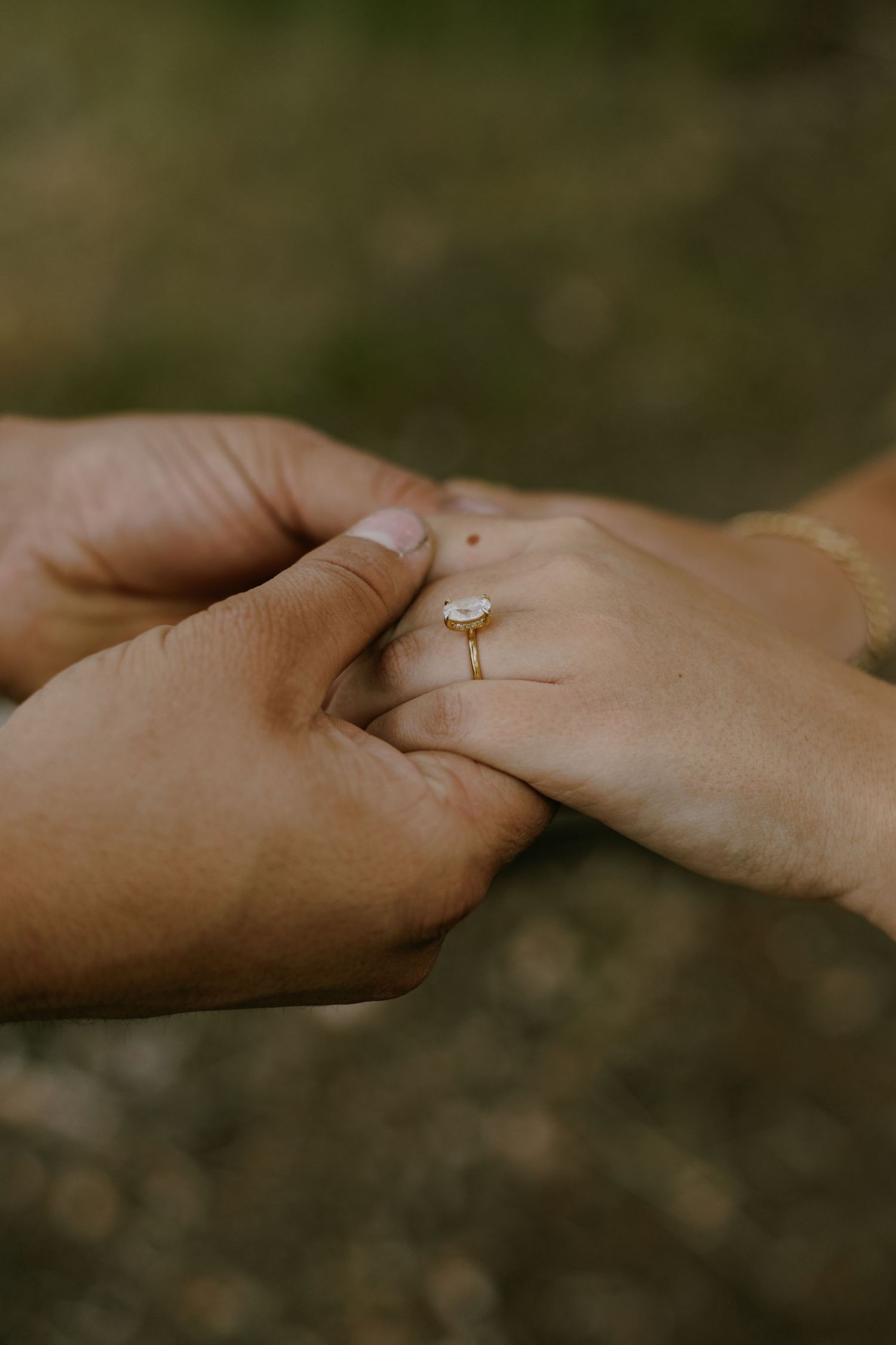 Two hands gently touching with an engagement ring visible in warm lighting.