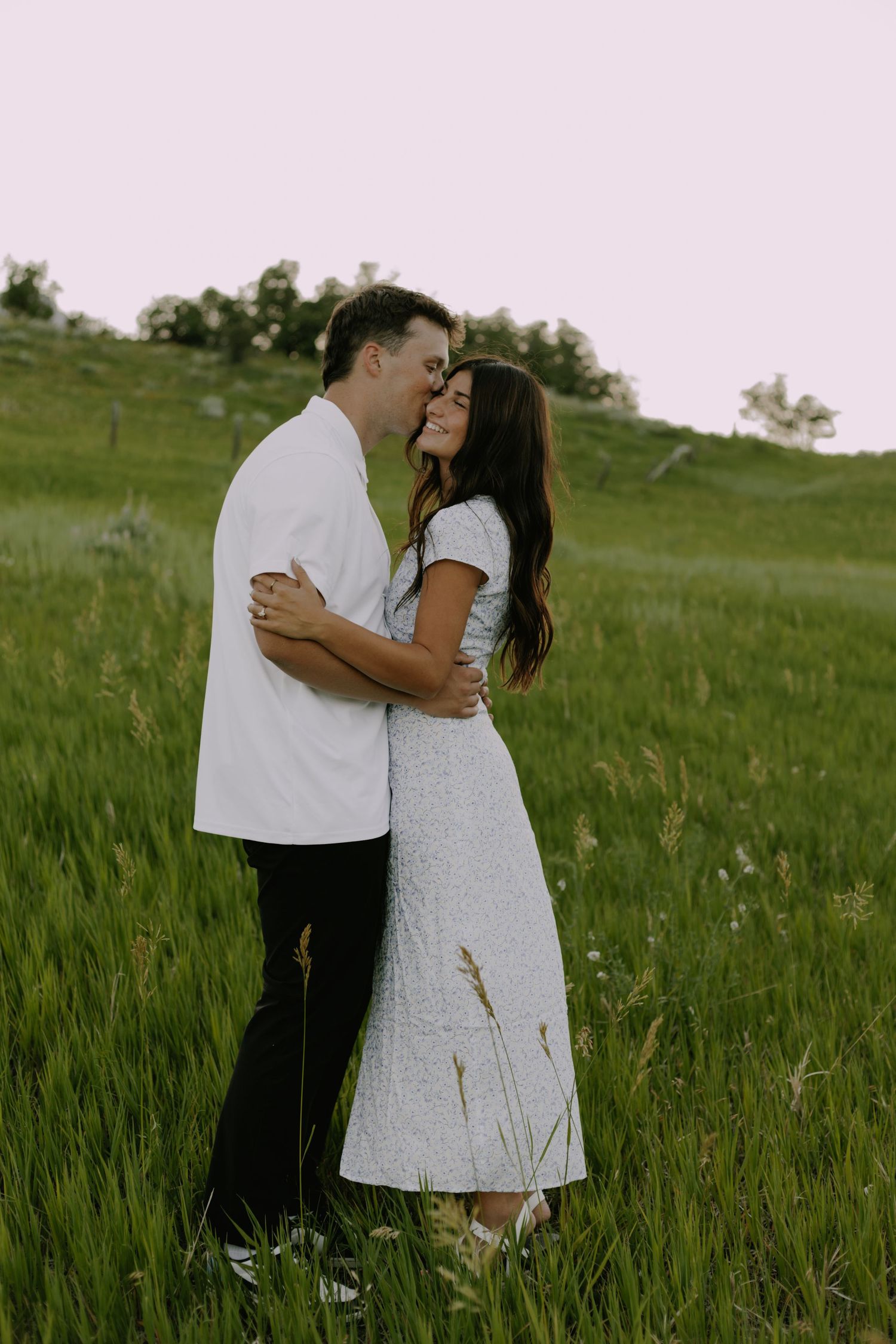 Couple in casual attire embraces tenderly in a sunlit meadow.