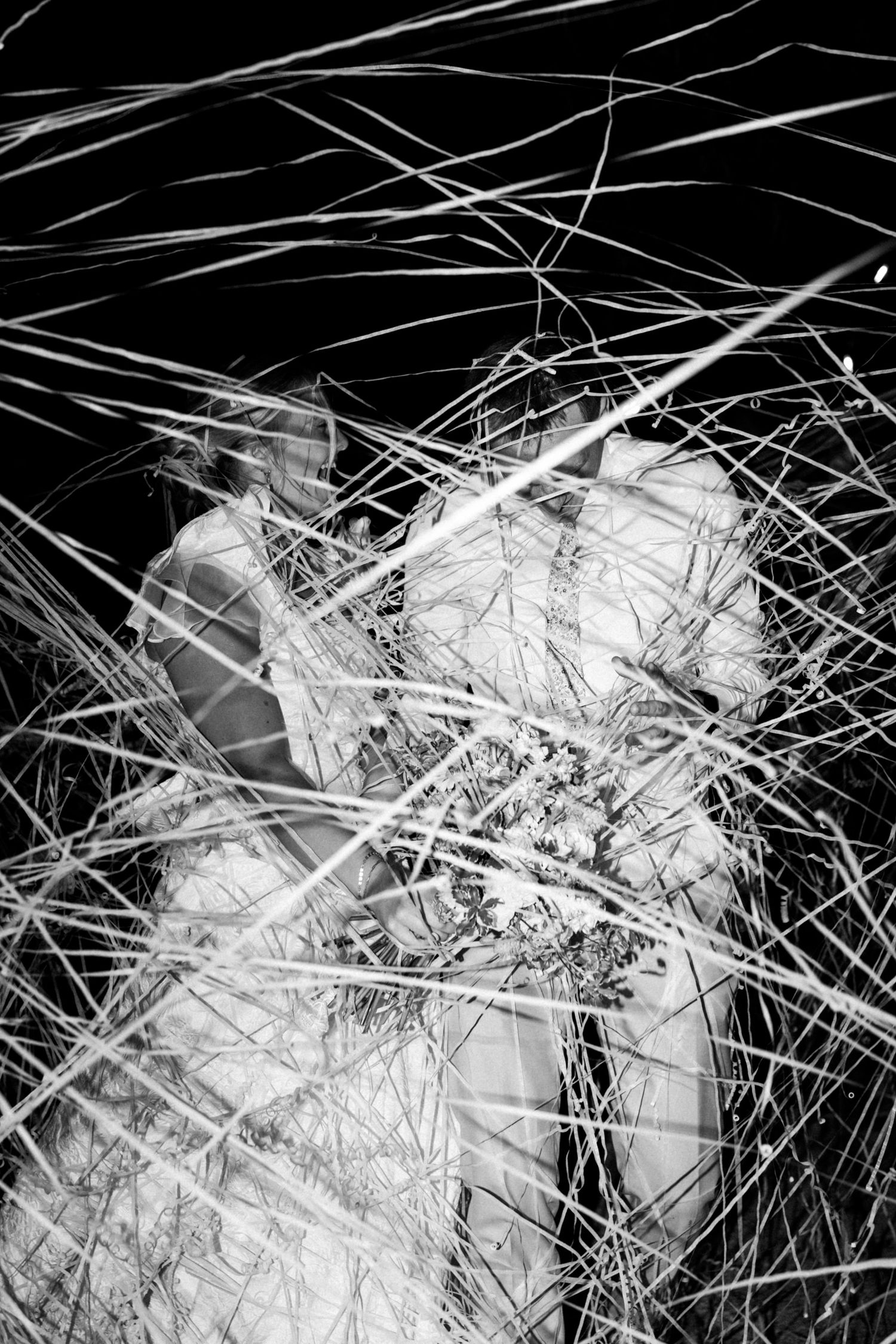 Artistic black and white shot of wedding attendees through overlapping grass stems.