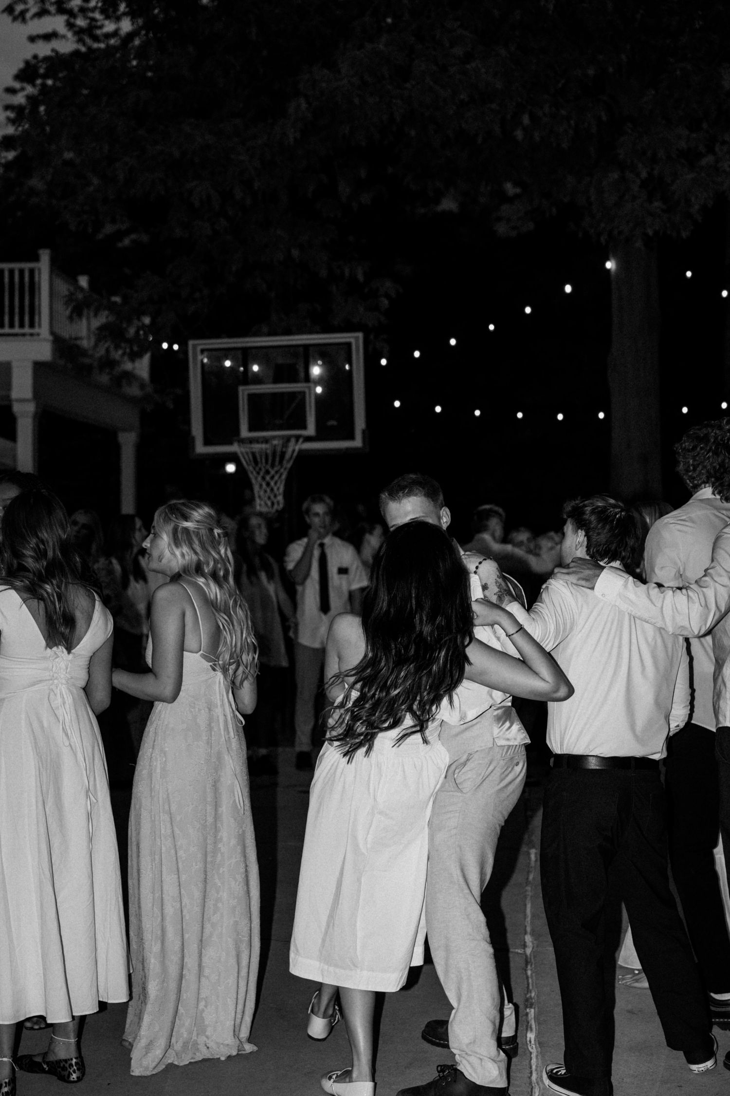 Large group of wedding guests dancing together in white attire at nighttime celebration.