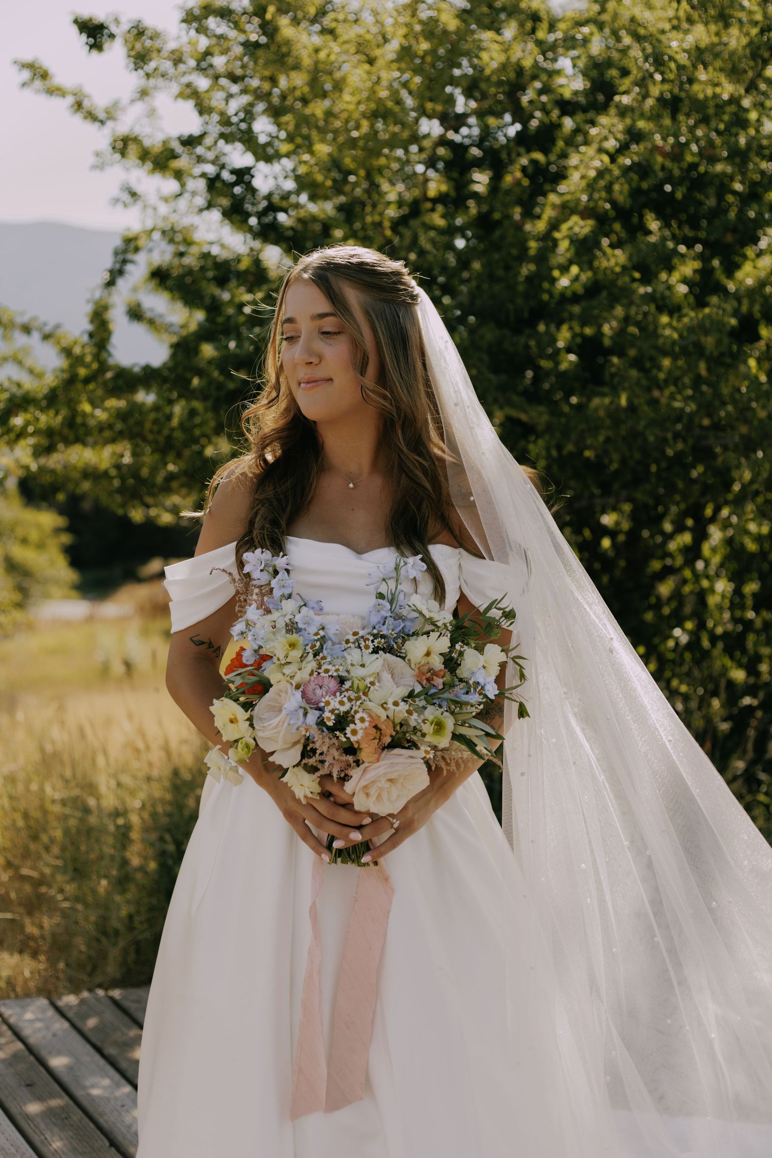 Close-up details of a bride in a white gown holding a pastel floral bouquet.