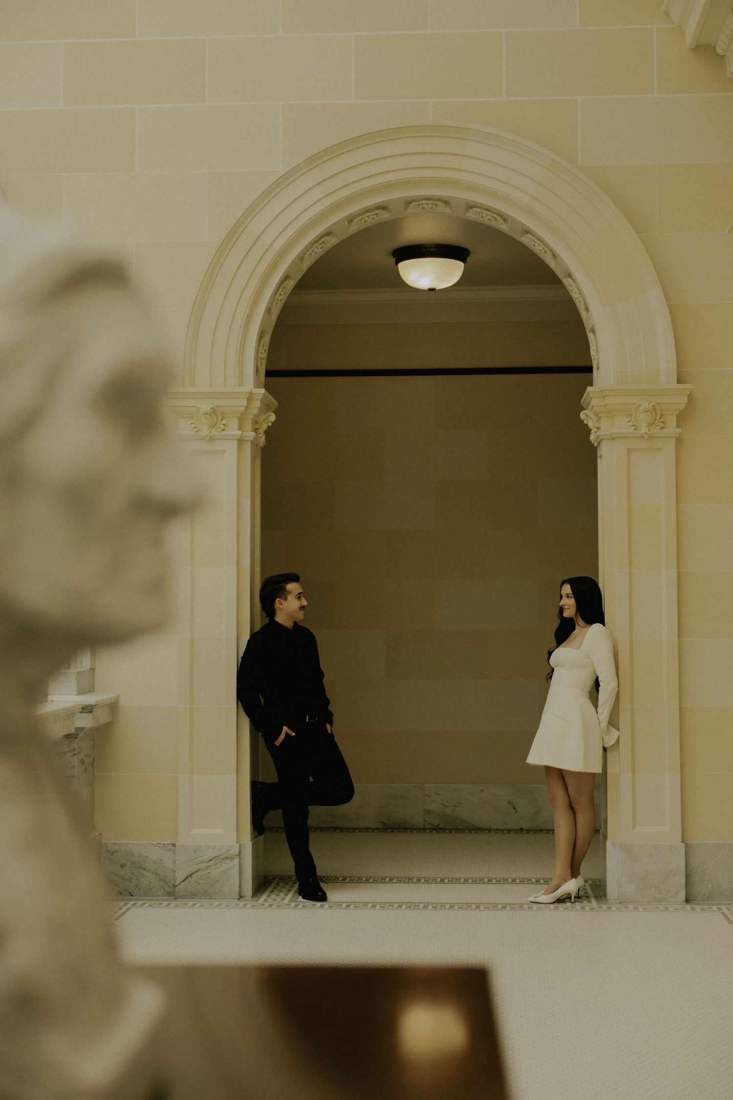 Two silhouettes meet under an elegant archway in a dramatic architectural setting.