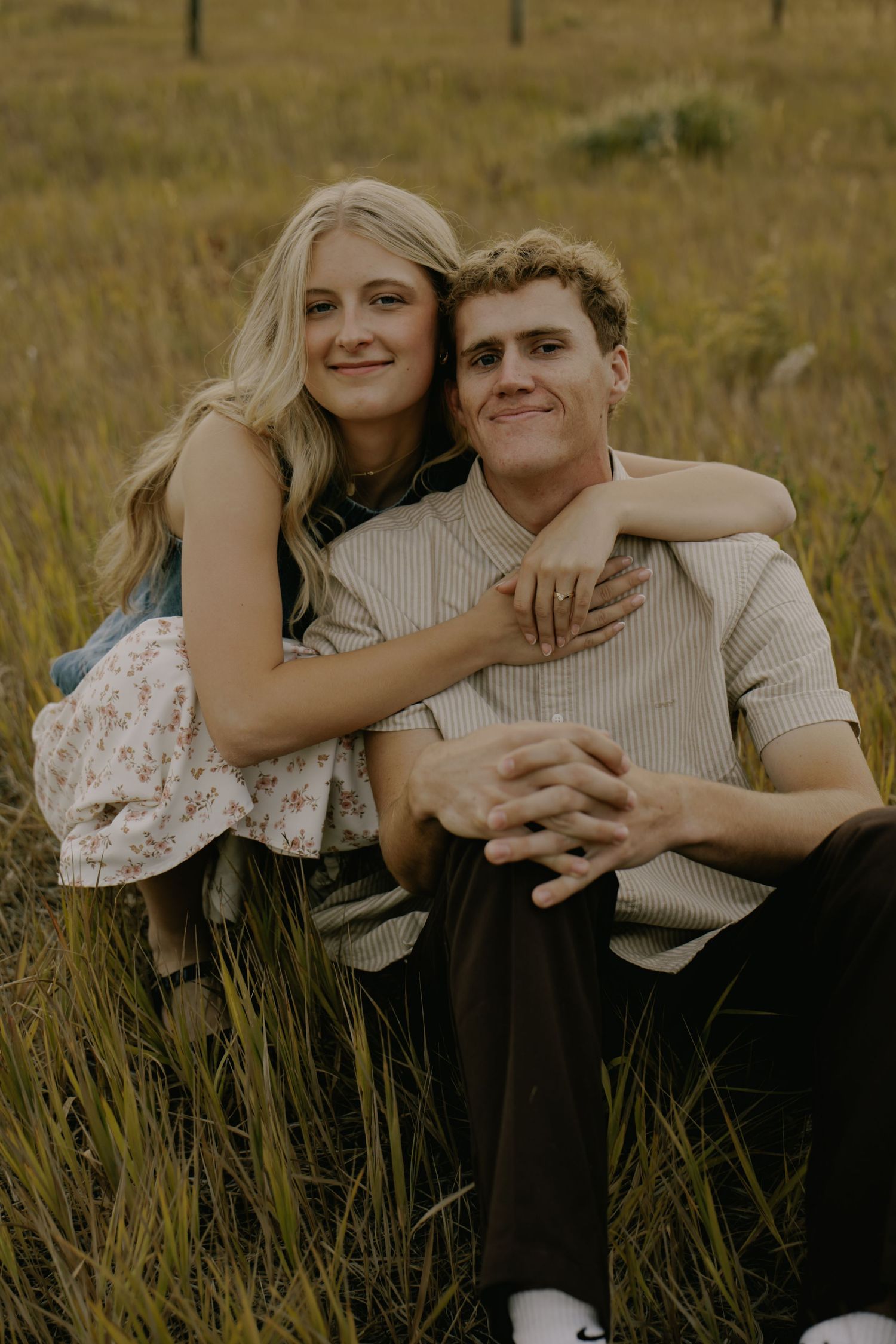 Couple shares tender moments while sitting together in tall grass during golden hour.