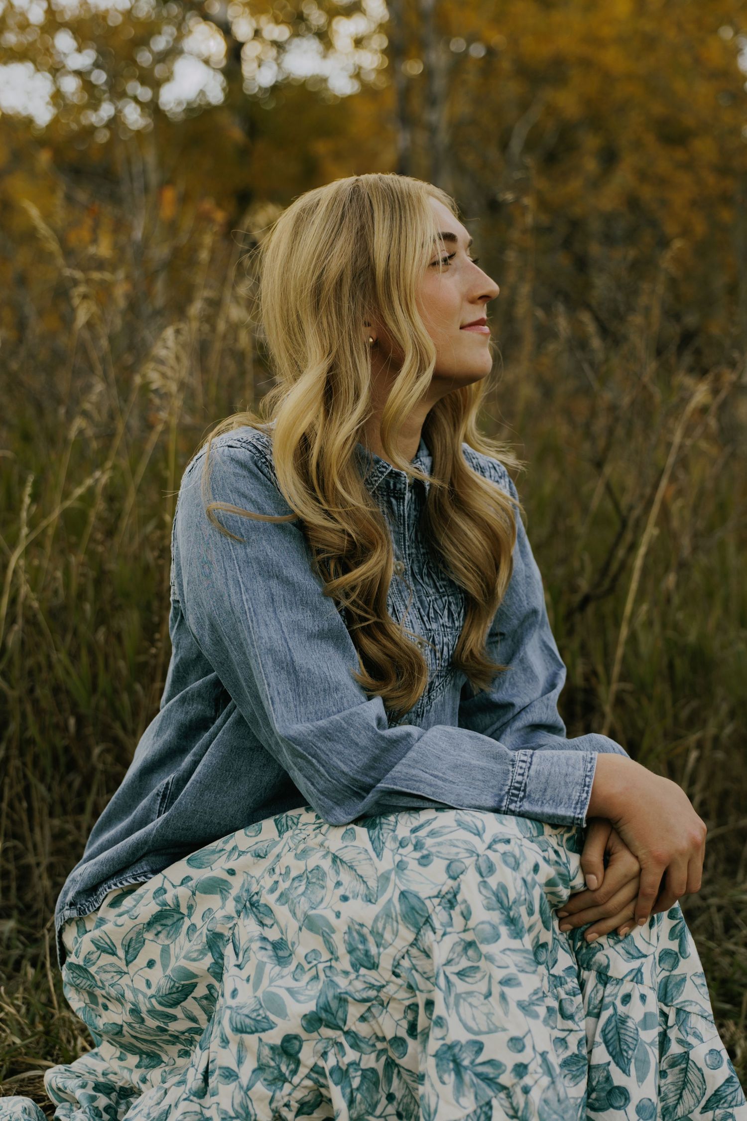 A denim jacket paired with a floral dress creates a casual look in an outdoor autumn setting.