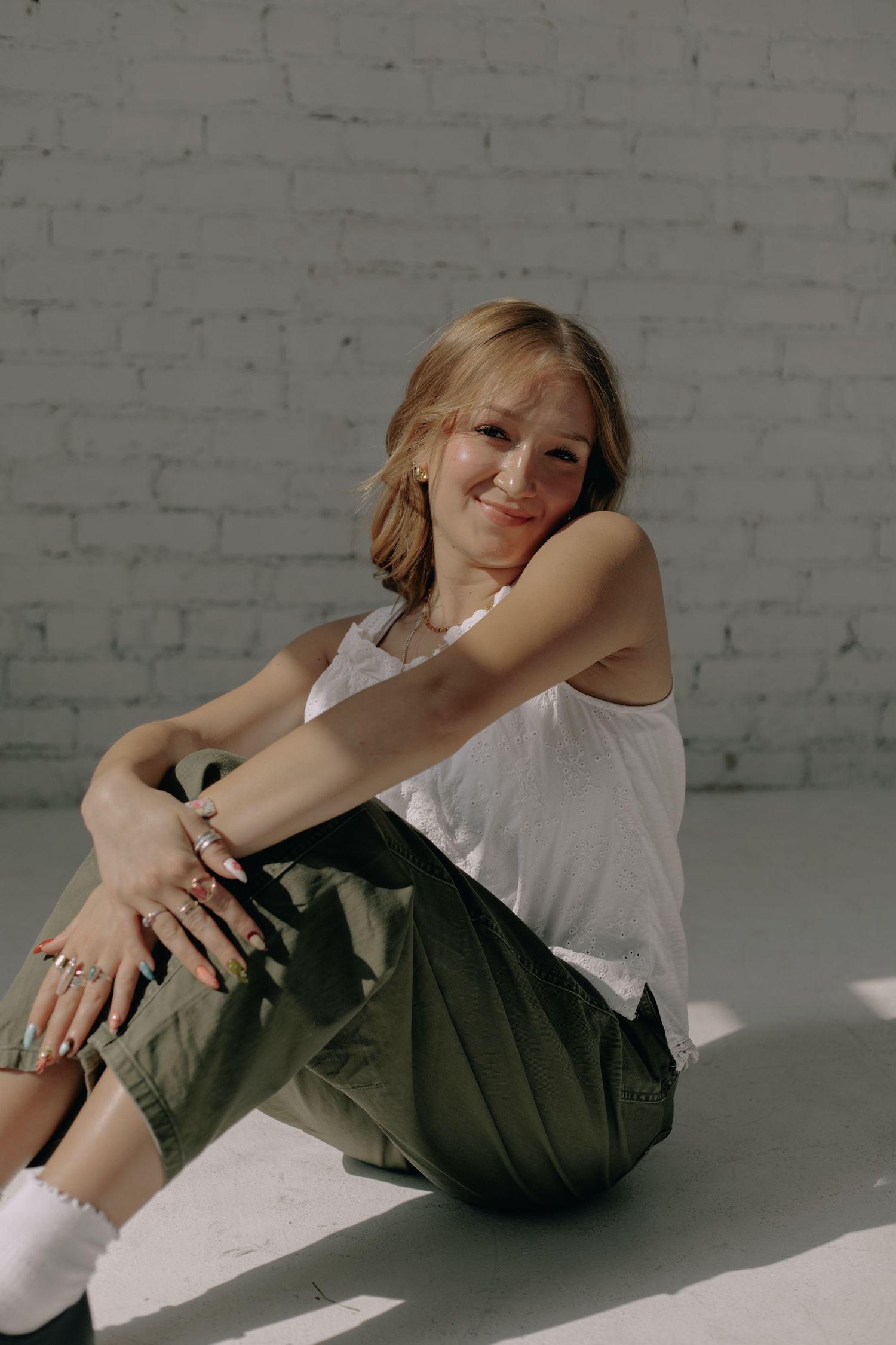 Casual lifestyle pose on white floor showing relaxed lounging against brick wall backdrop.