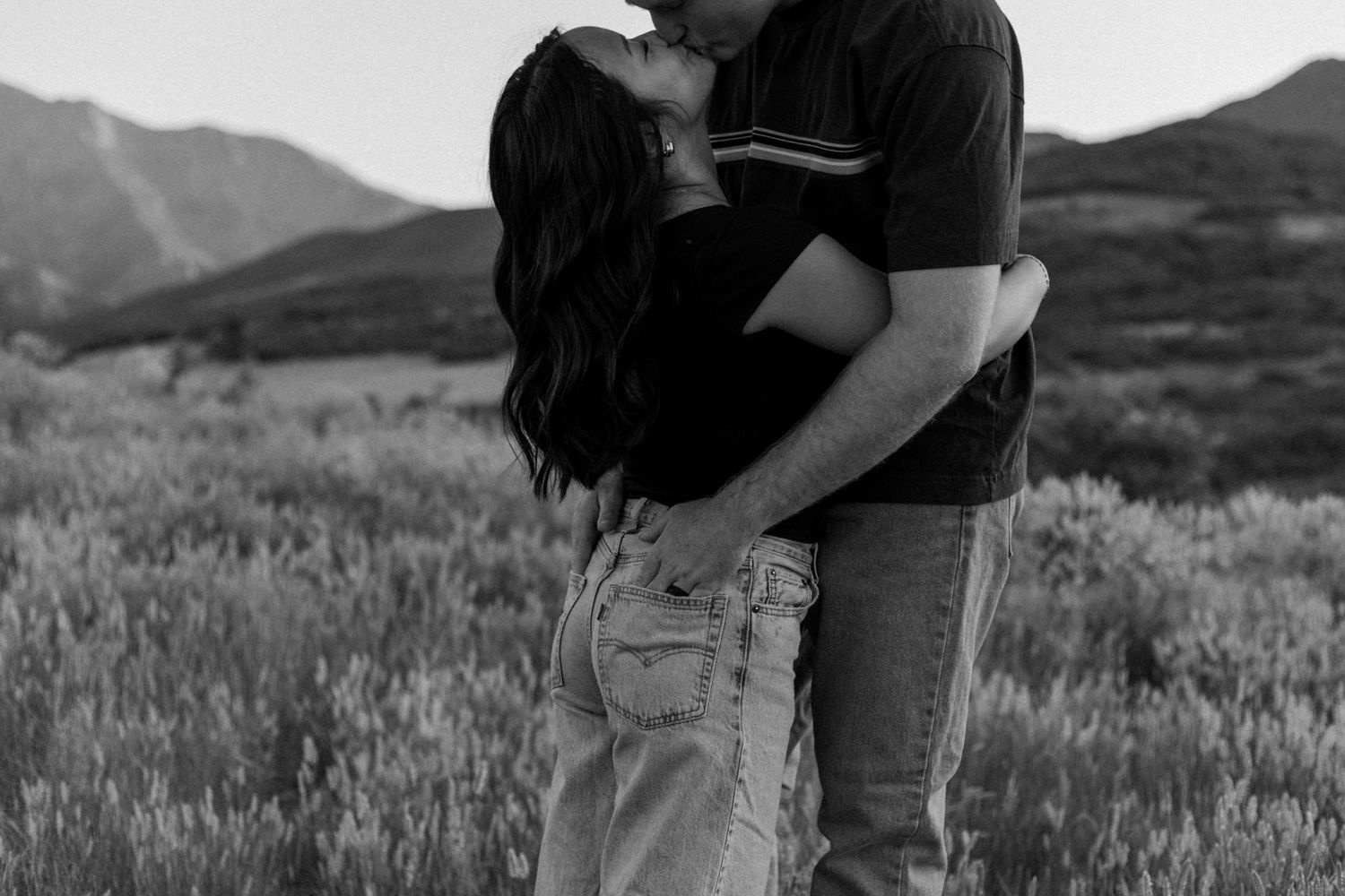 A romantic couple embraces in a mountain meadow during golden hour.
