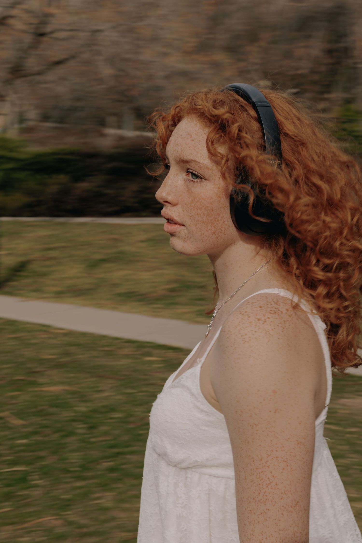 Figure with flowing red hair wearing white dress in outdoor setting.