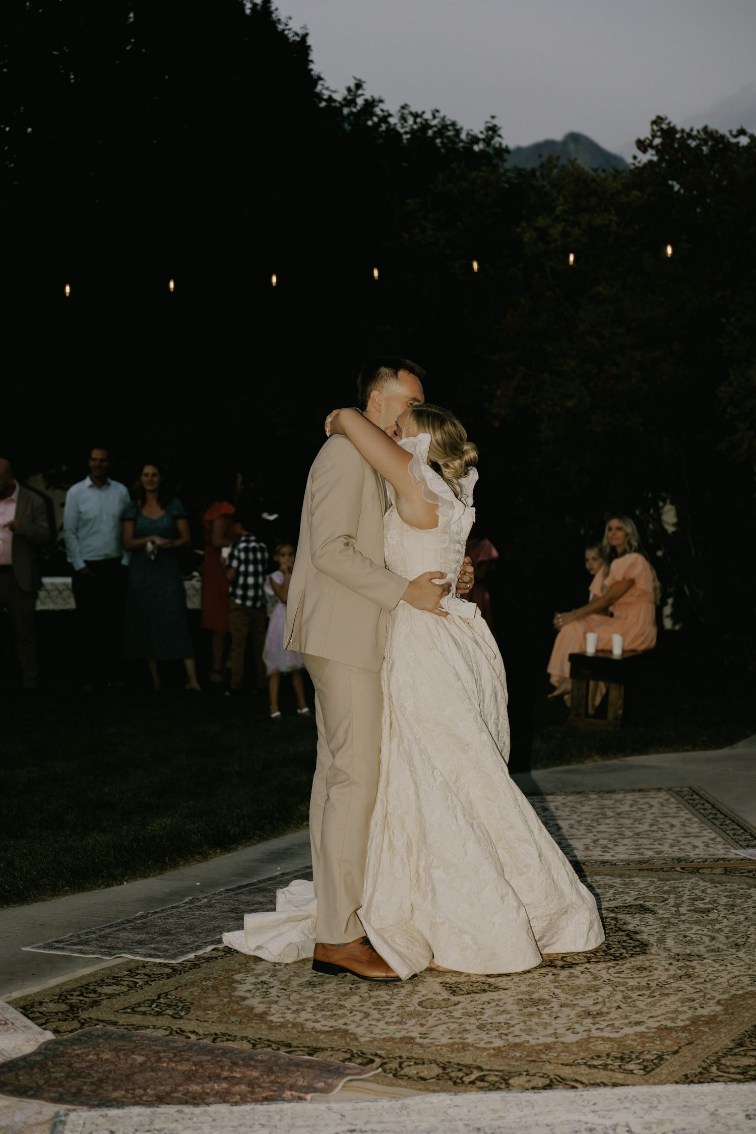 A romantic dance moment captured on an outdoor rug during an evening wedding reception.